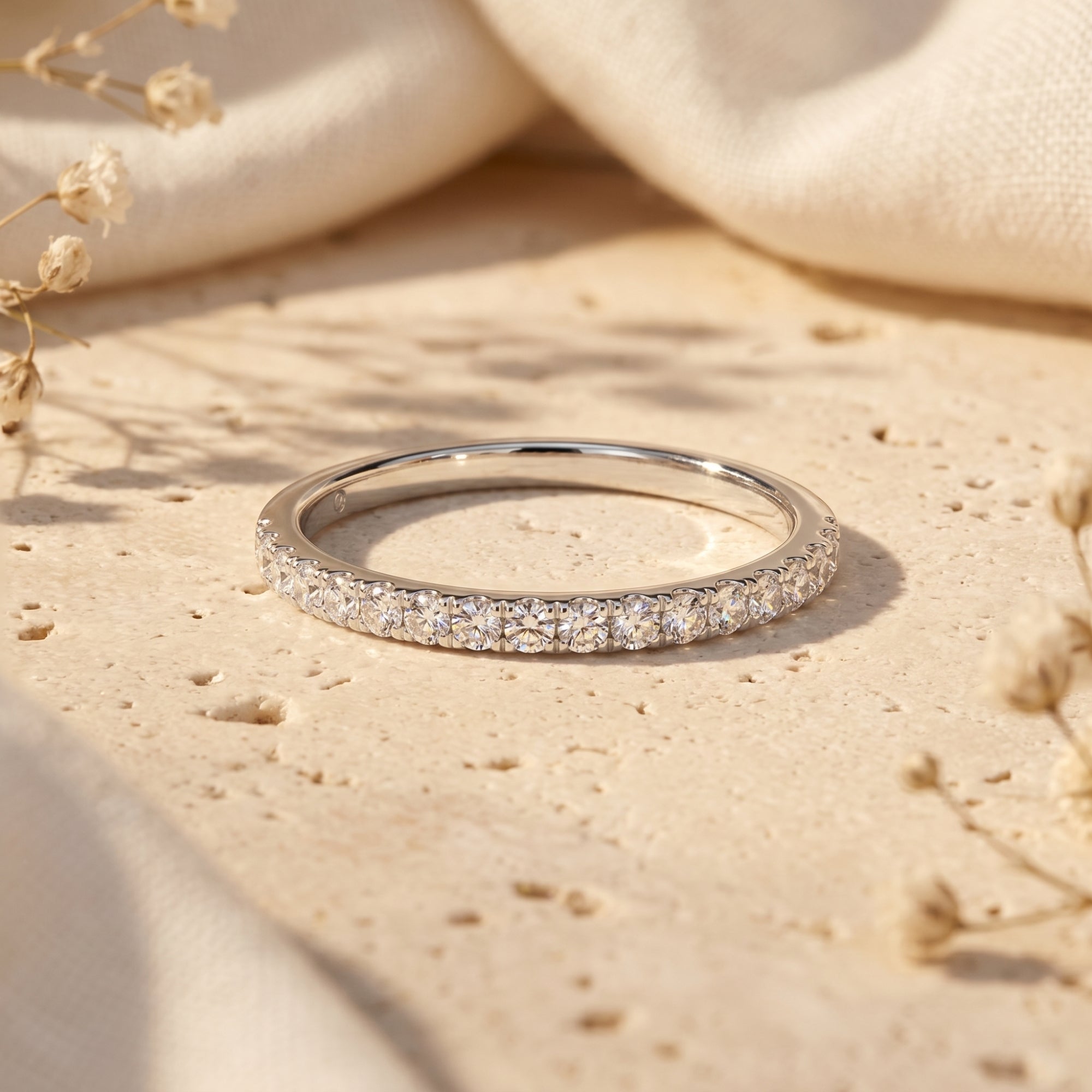 Sylvienne moissanite pave band in S925 sterling silver on a textured stone surface with dried flowers.