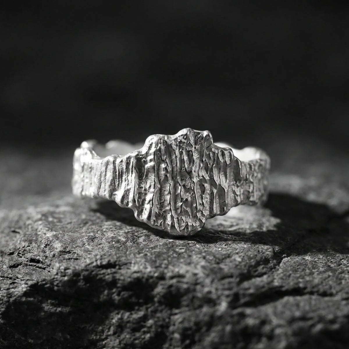 Front view of a silver ring with deeply sculpted bark texture resting on dark stone.