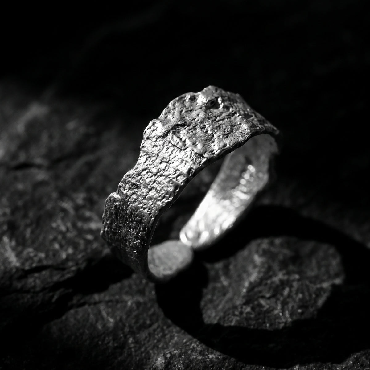 Angled close-up of a textured silver open-band ring standing on dark stone.