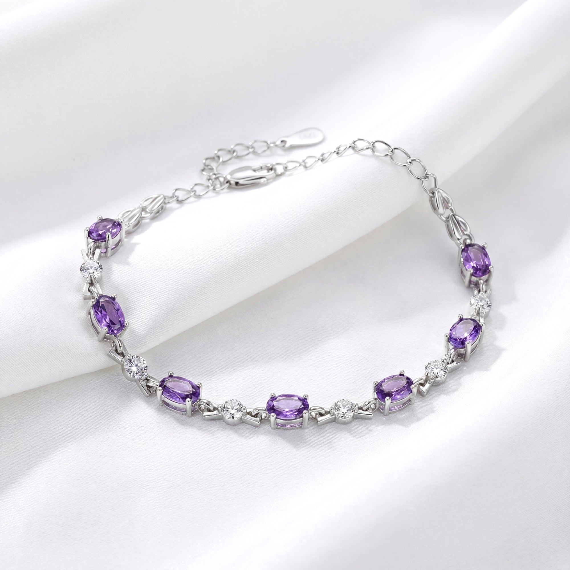 Sterling silver bracelet featuring oval simulated amethyst and round stones on a draped white fabric background.