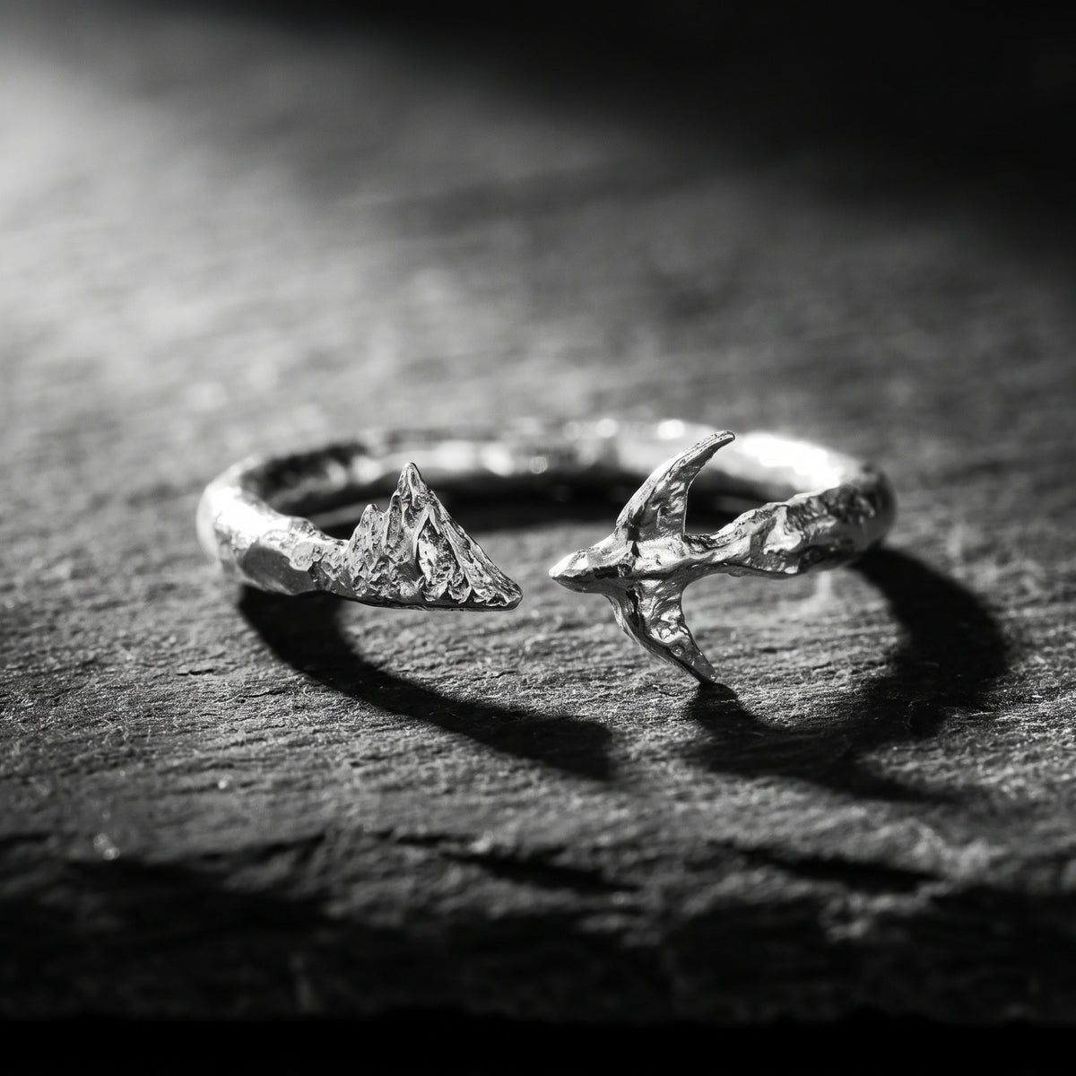 Front view of a silver open-band ring with carved mountain and soaring bird motifs on a dark stone surface.