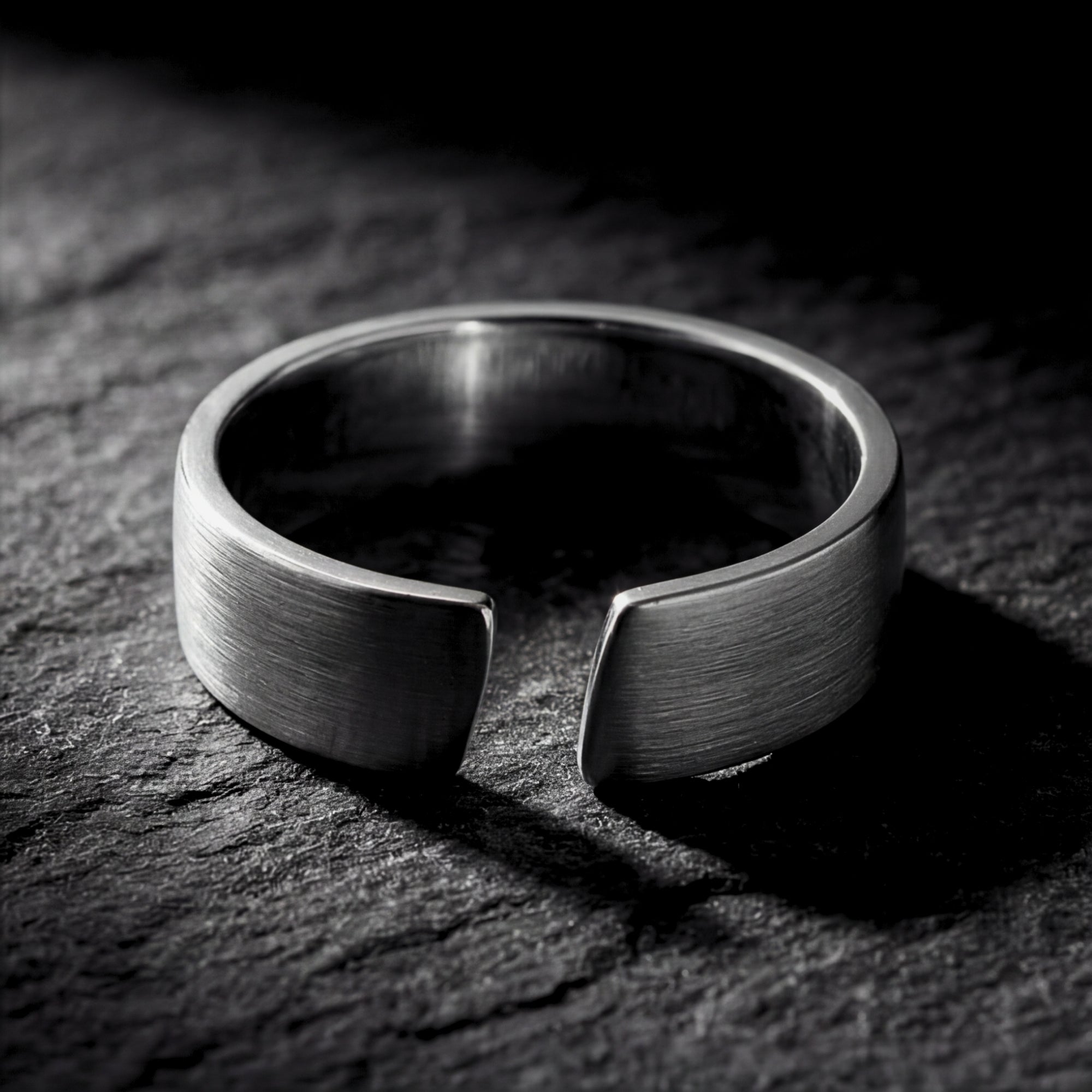 Brushed silver stainless steel Spartan band ring with an open cuff design on a dark textured stone surface.