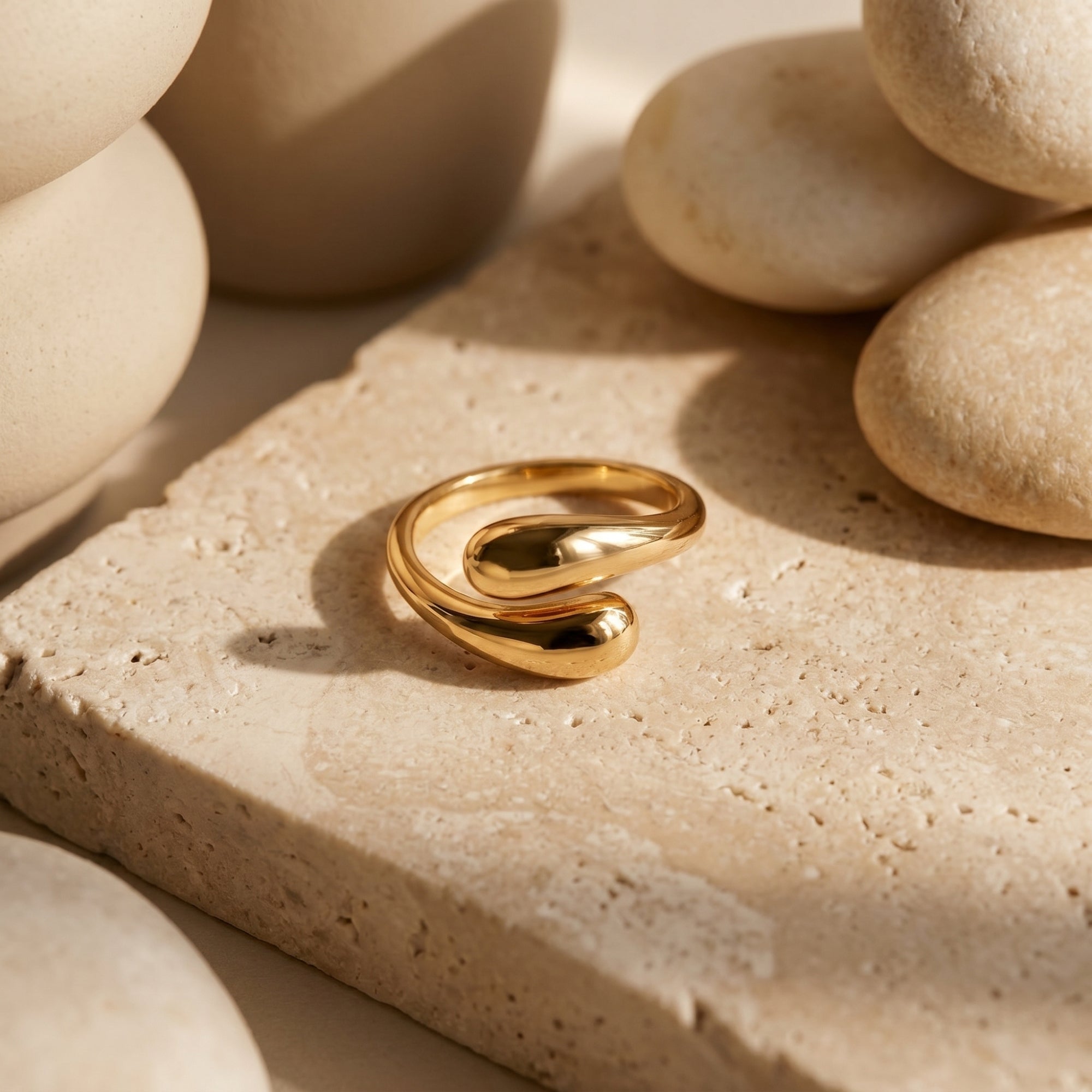 Gold vermeil bypass ring with organic curves on a textured stone surface with river rocks.