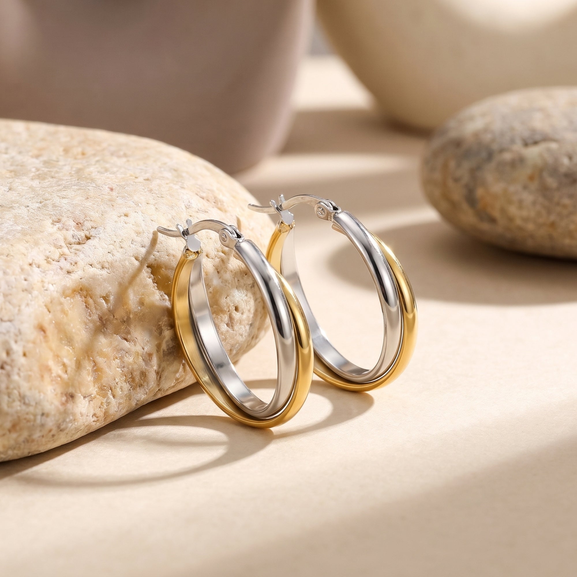 Two-tone gold and silver interlocking huggie earrings on a natural stone background.