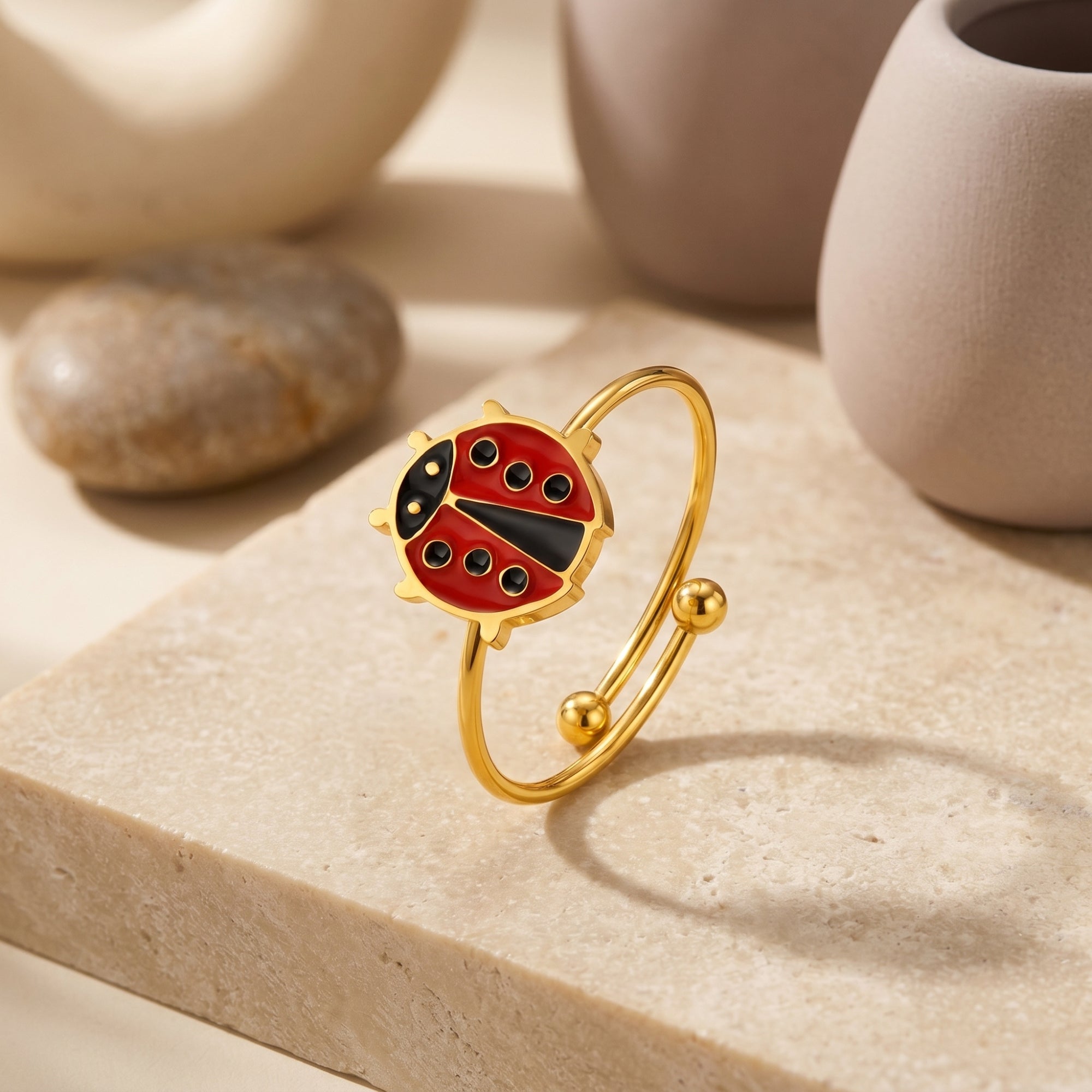 Gold ladybug bypass ring with red enamel on a stone slab with props.