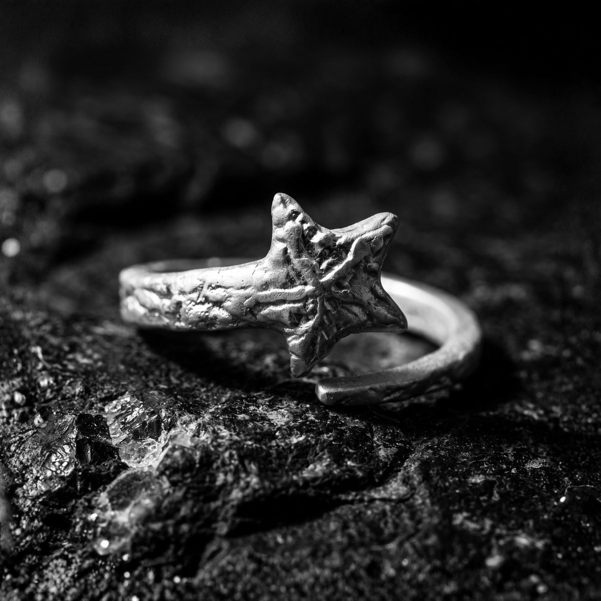 Textured silver star open ring resting on a dark rock surface in a close-up view.
