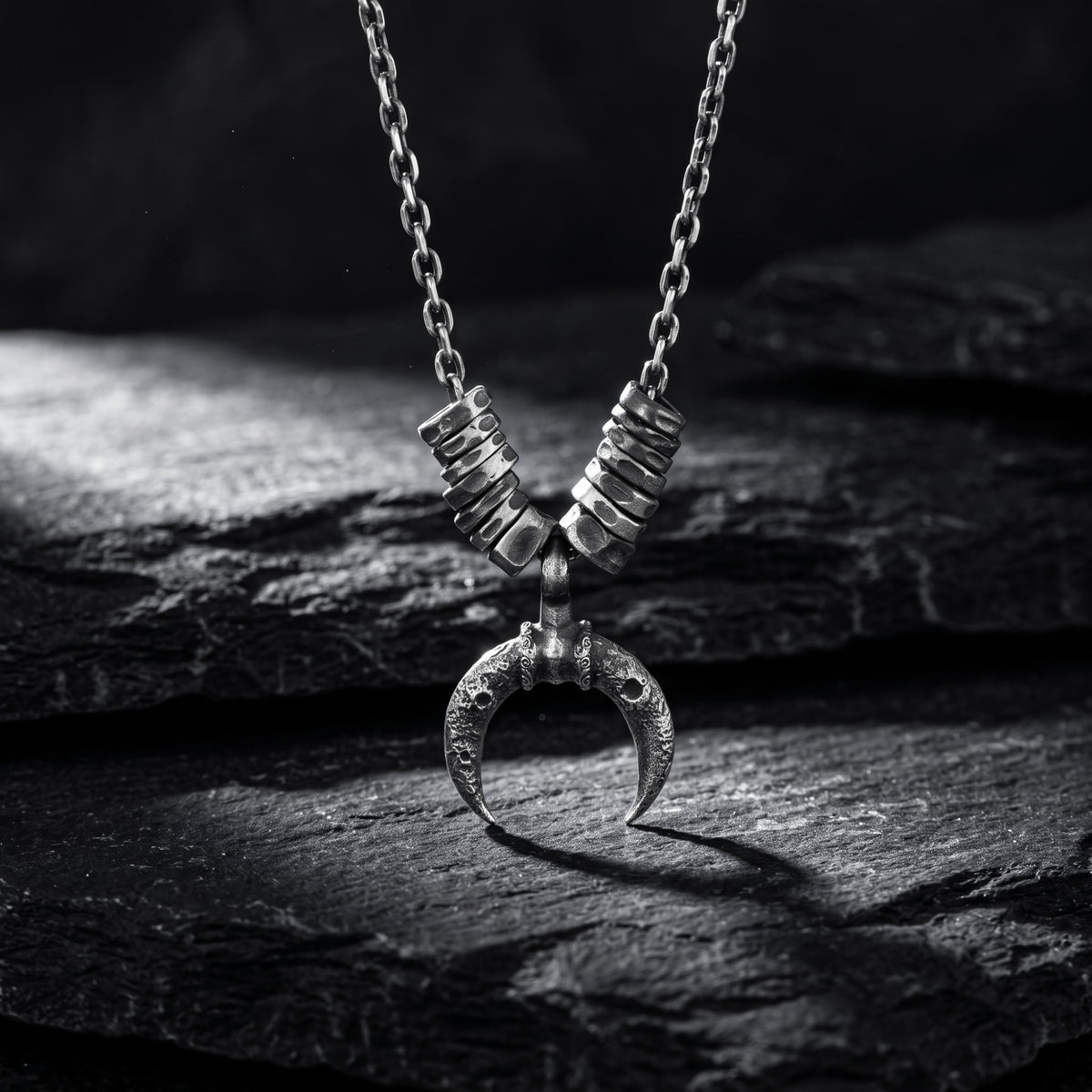 Crescent pendant necklace with textured segmented spacers, hanging upright over dark slate.