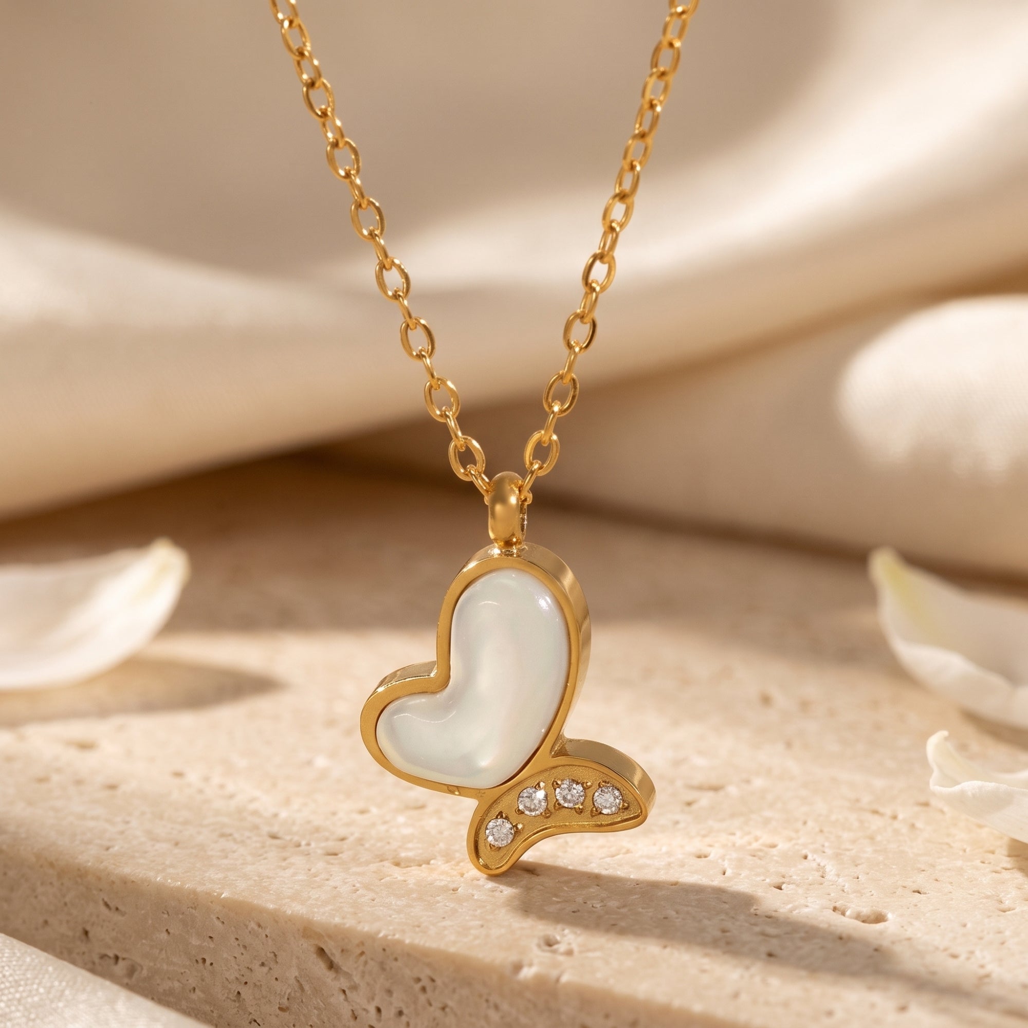 Gold butterfly pendant with mother of pearl inlay and cubic zirconia accents on a textured stone surface.