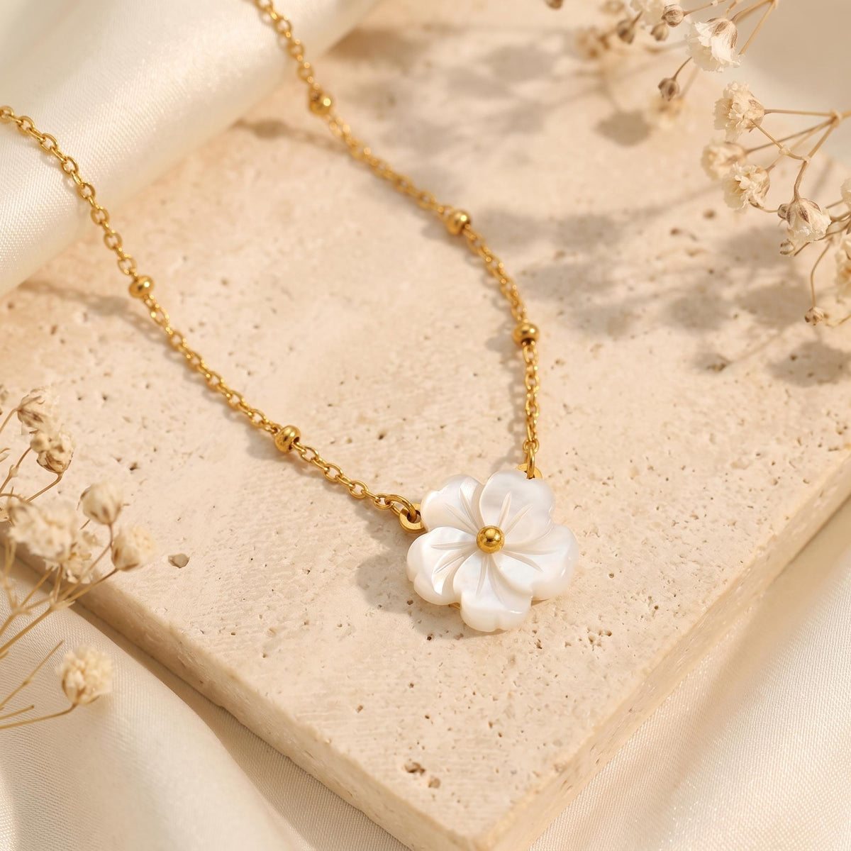 Gold-tone bead-station necklace with a carved white flower pendant resting on a beige stone surface.