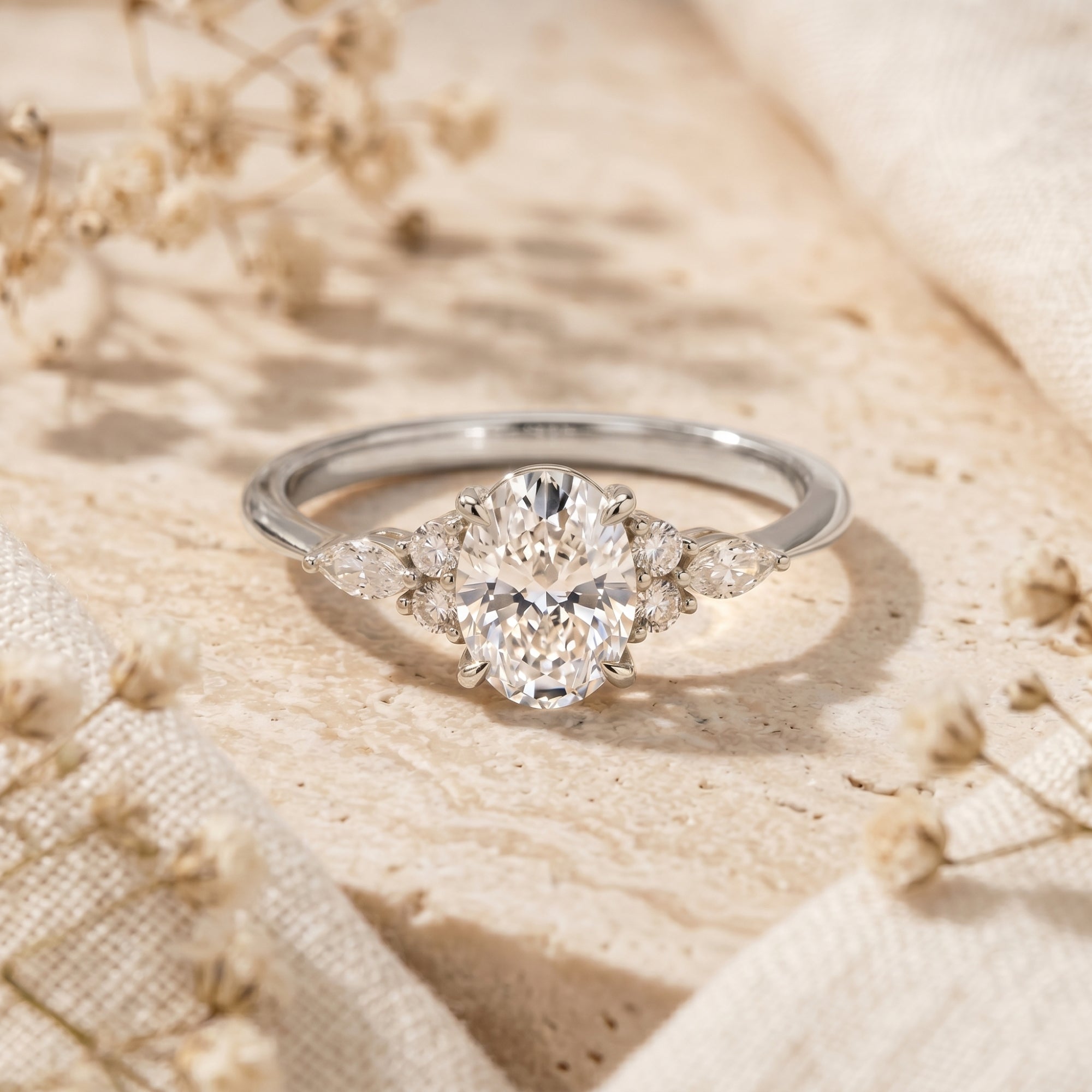 Silver oval moissanite promise ring on a stone surface with dried flowers.