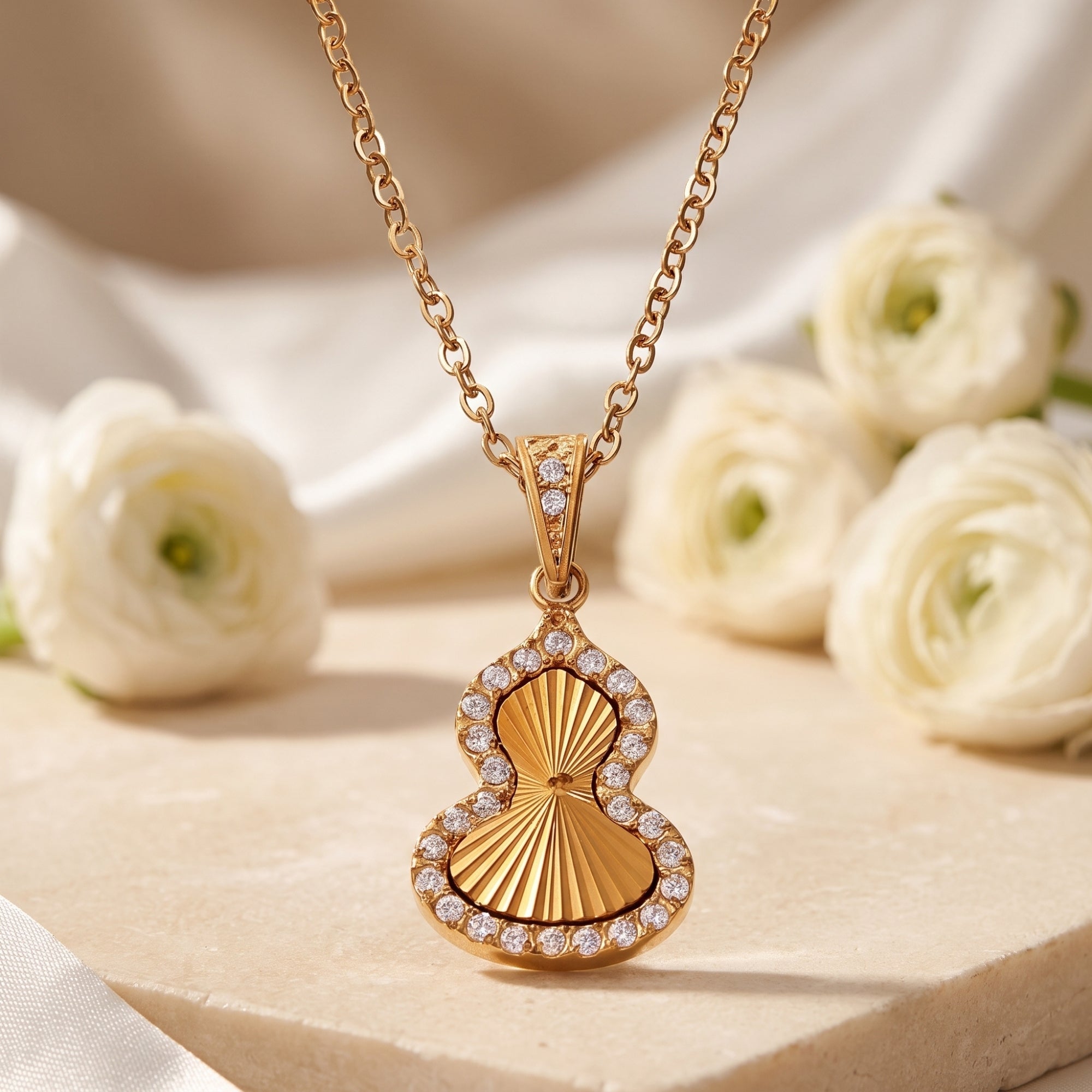Gold gourd pendant necklace with cubic zirconia halo on stone surface with white flowers.