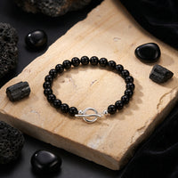 Natural 6mm black onyx bead bracelet with a silver toggle clasp resting on a tan stone slab in a styled setting.
