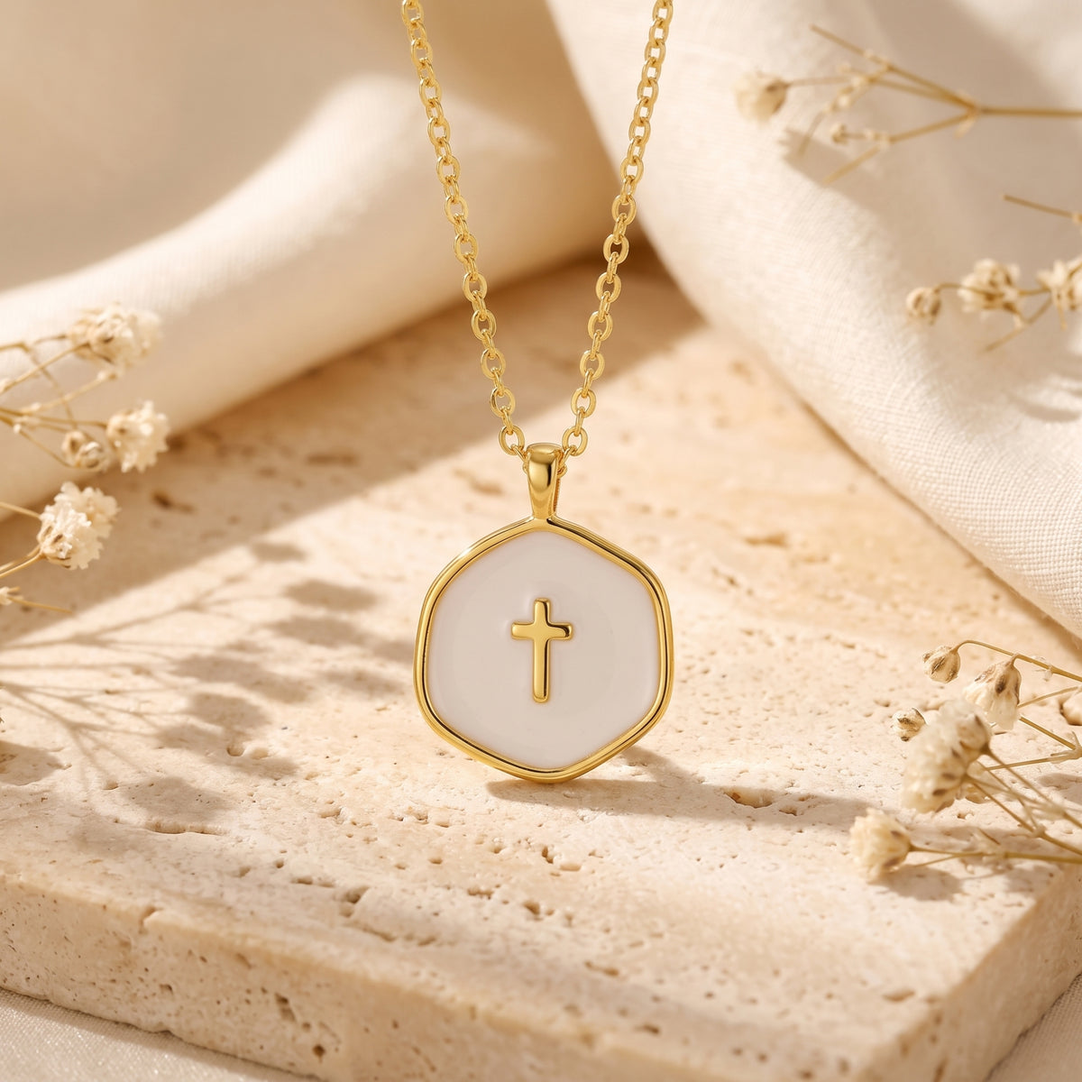 Close-up of a gold-tone shield-shaped pendant necklace with white enamel inlay and a raised cross on a stone surface.