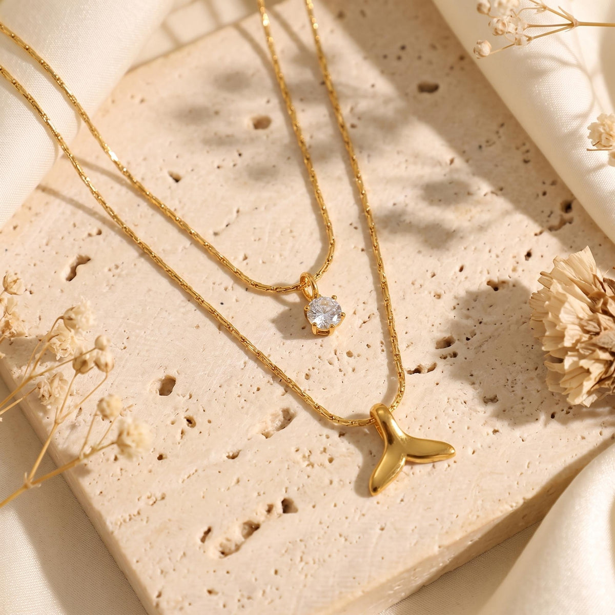 Gold-tone double-layered necklace on stone featuring a clear crystal solitaire and whale tail pendant.