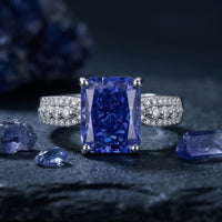 Radiant cut natural tanzanite ring in sterling silver on a dark textured background with raw gemstones.