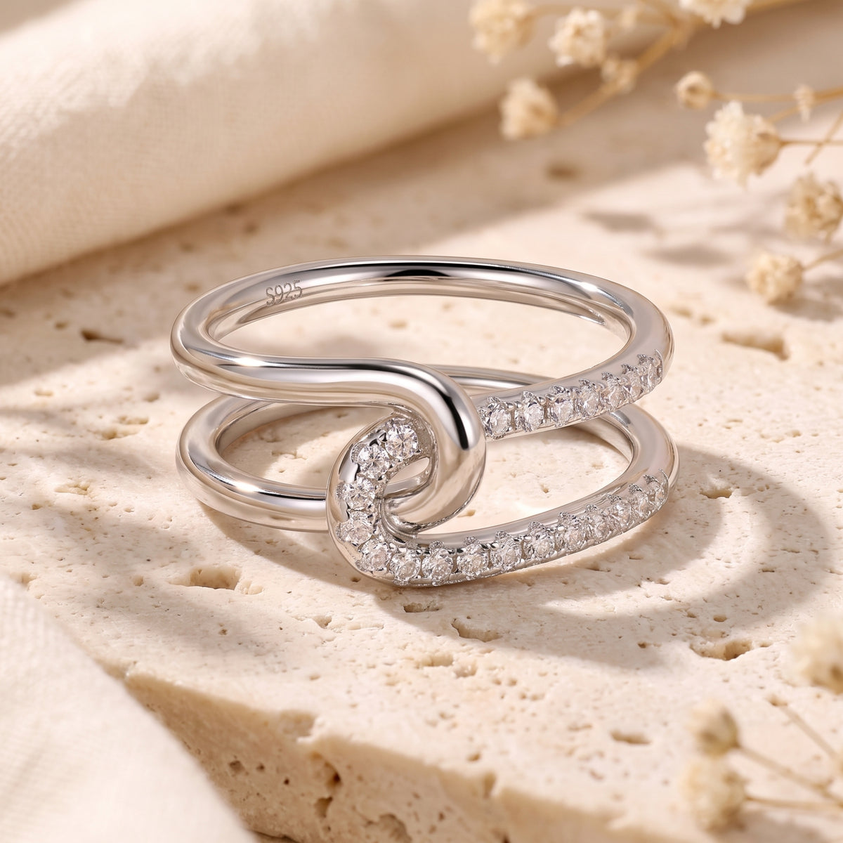 Close-up of a silver double-band interlocking knot ring with cubic zirconia on a stone surface.