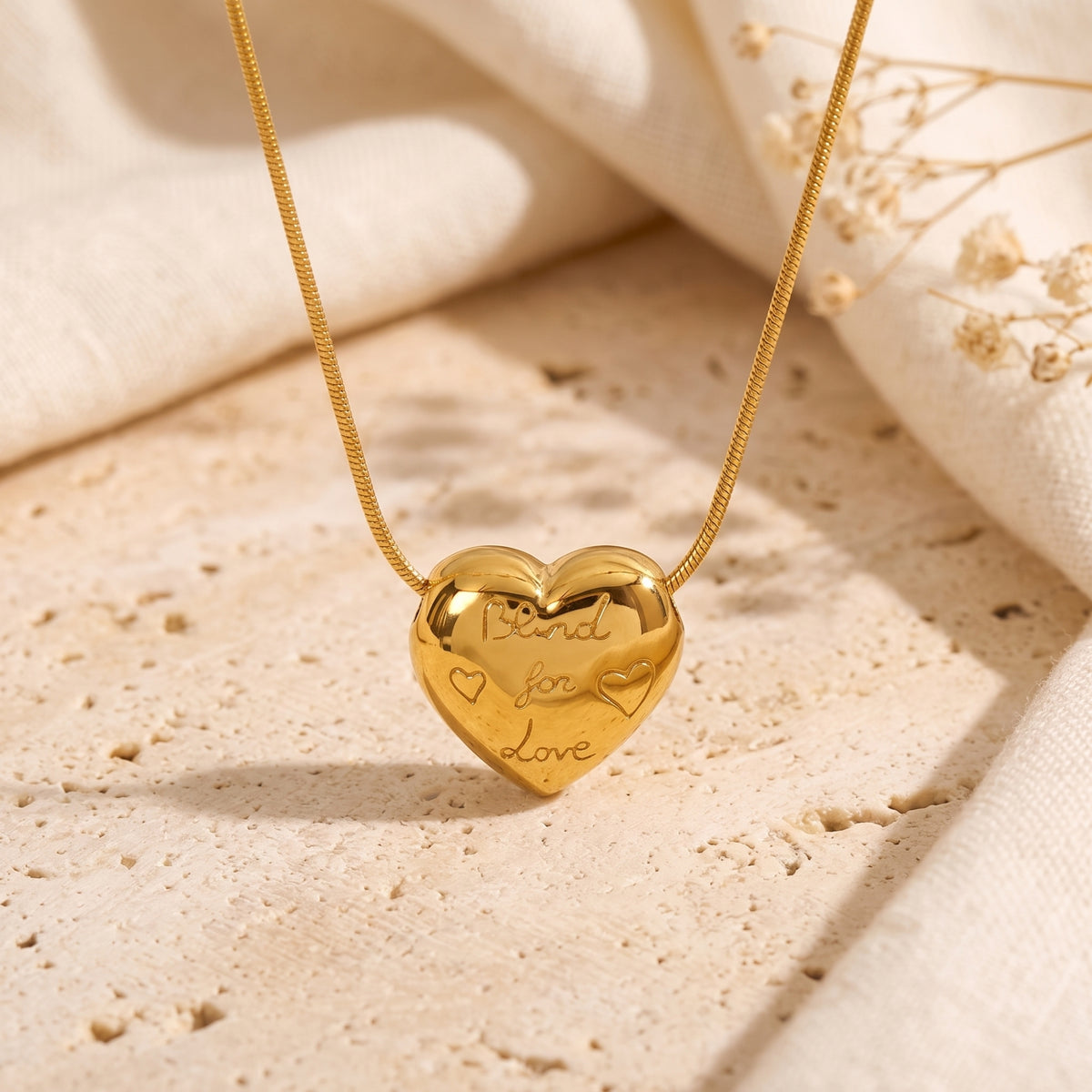 Close-up of a gold-tone puffed heart pendant engraved “Bond for Love” on a textured stone surface.