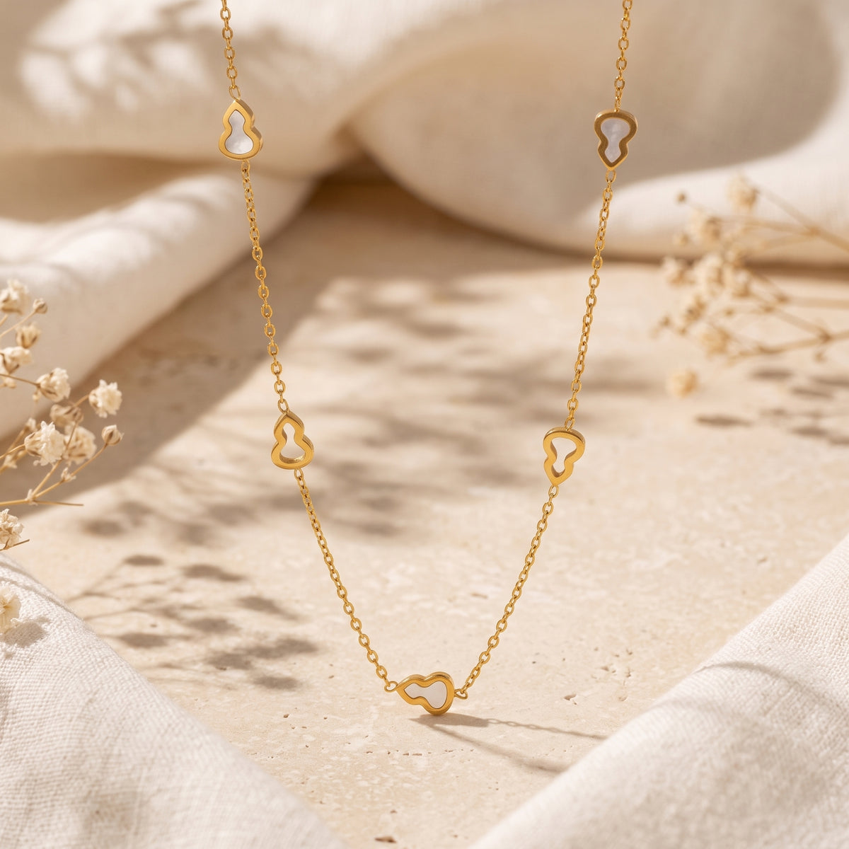 Gold-tone station necklace with white inlay gourd motifs displayed over a soft-toned stone and fabric setting.