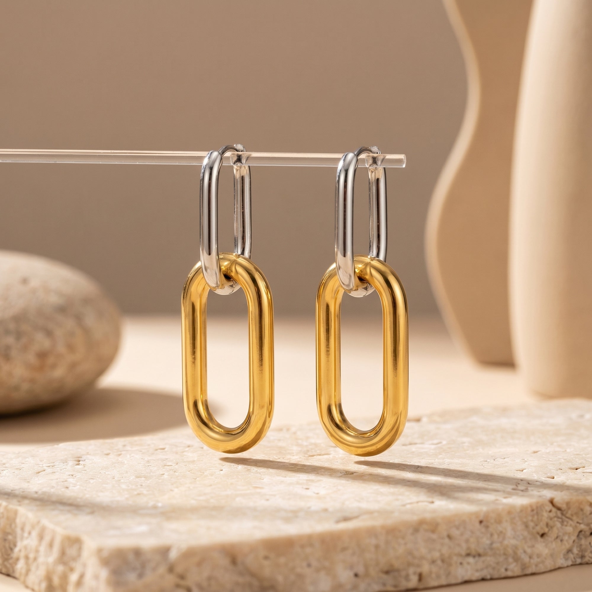 Two-tone silver and gold stainless steel drop earrings on a stone lifestyle display.