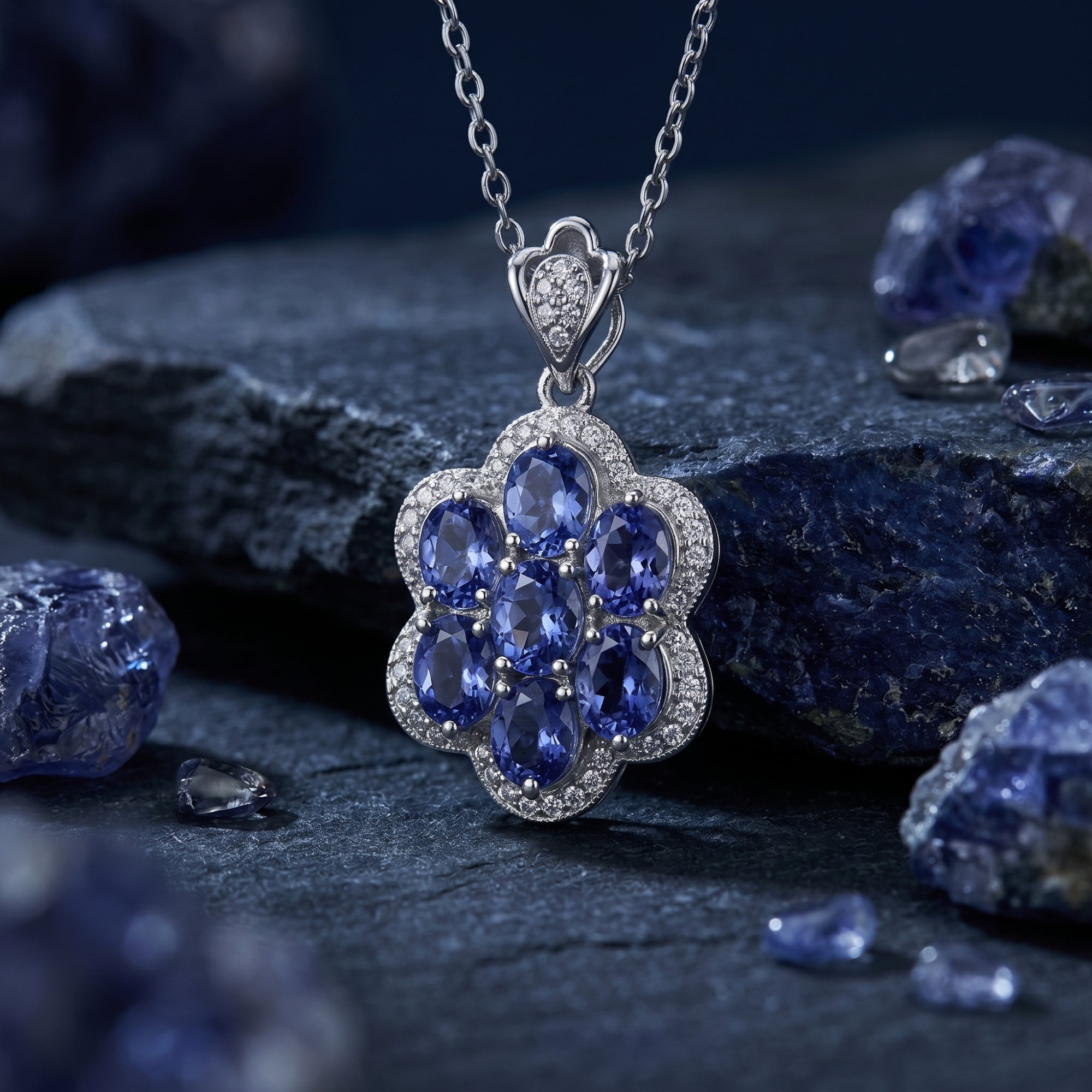 Oval tanzanite floral cluster pendant in sterling silver, styled on dark rocks with raw tanzanite crystals.