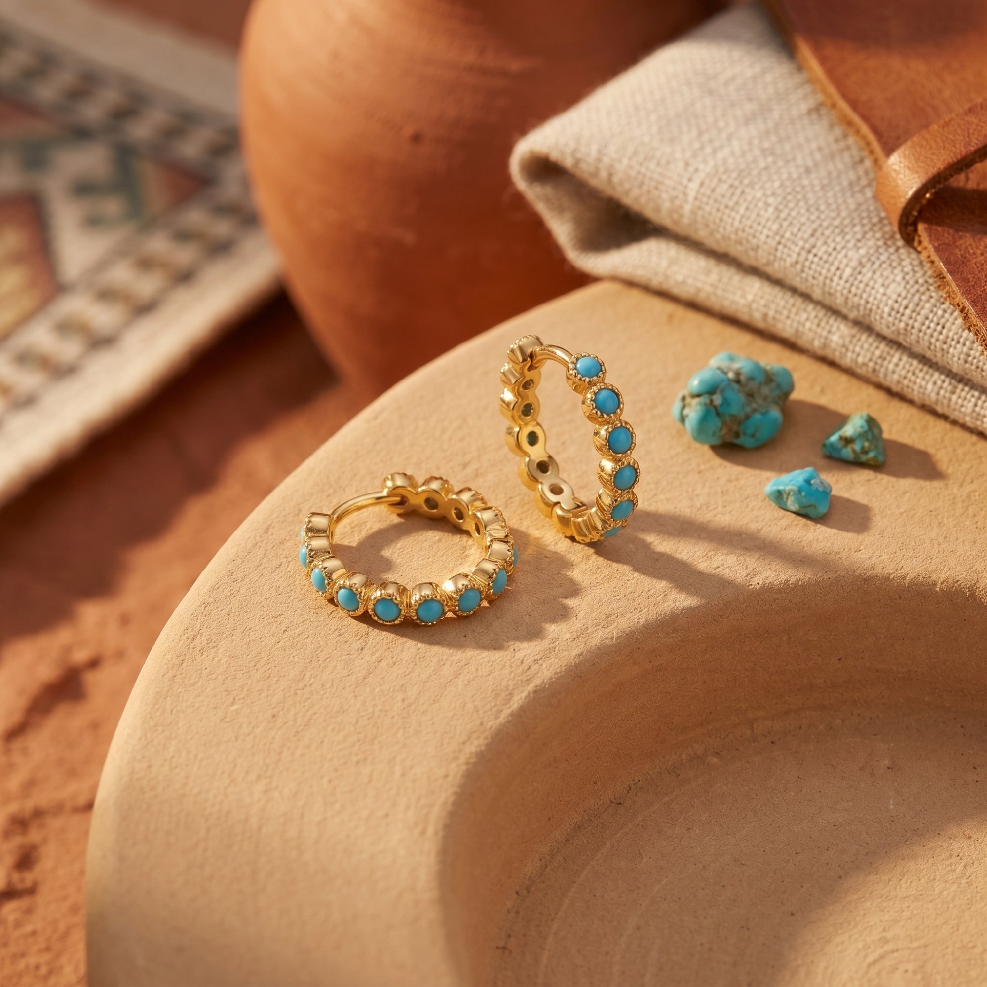 Gold vermeil huggie earrings with round turquoise cabochons on a desert-themed lifestyle background.