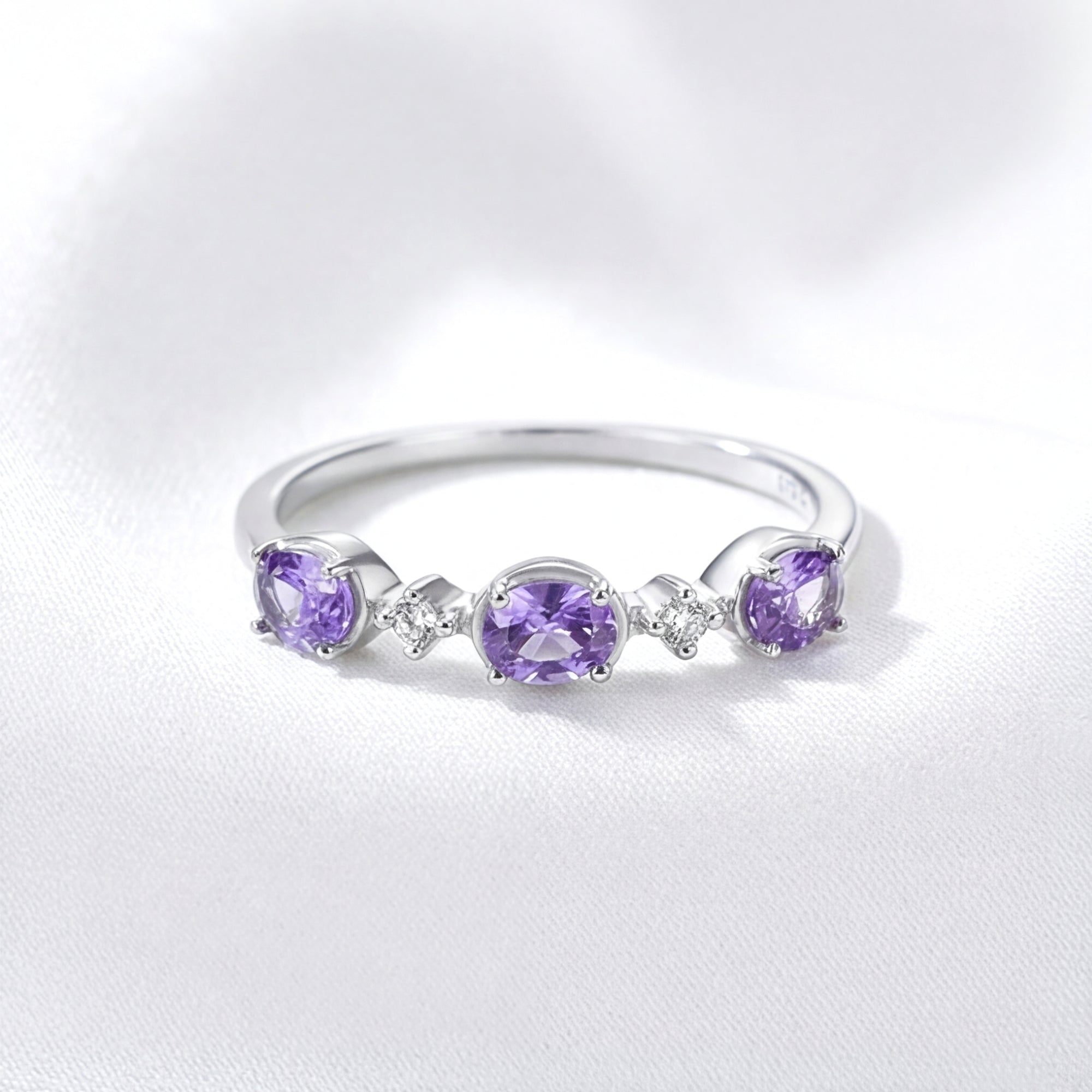 Serenitas S925 sterling silver ring with three oval-cut simulated amethyst stones on white fabric.