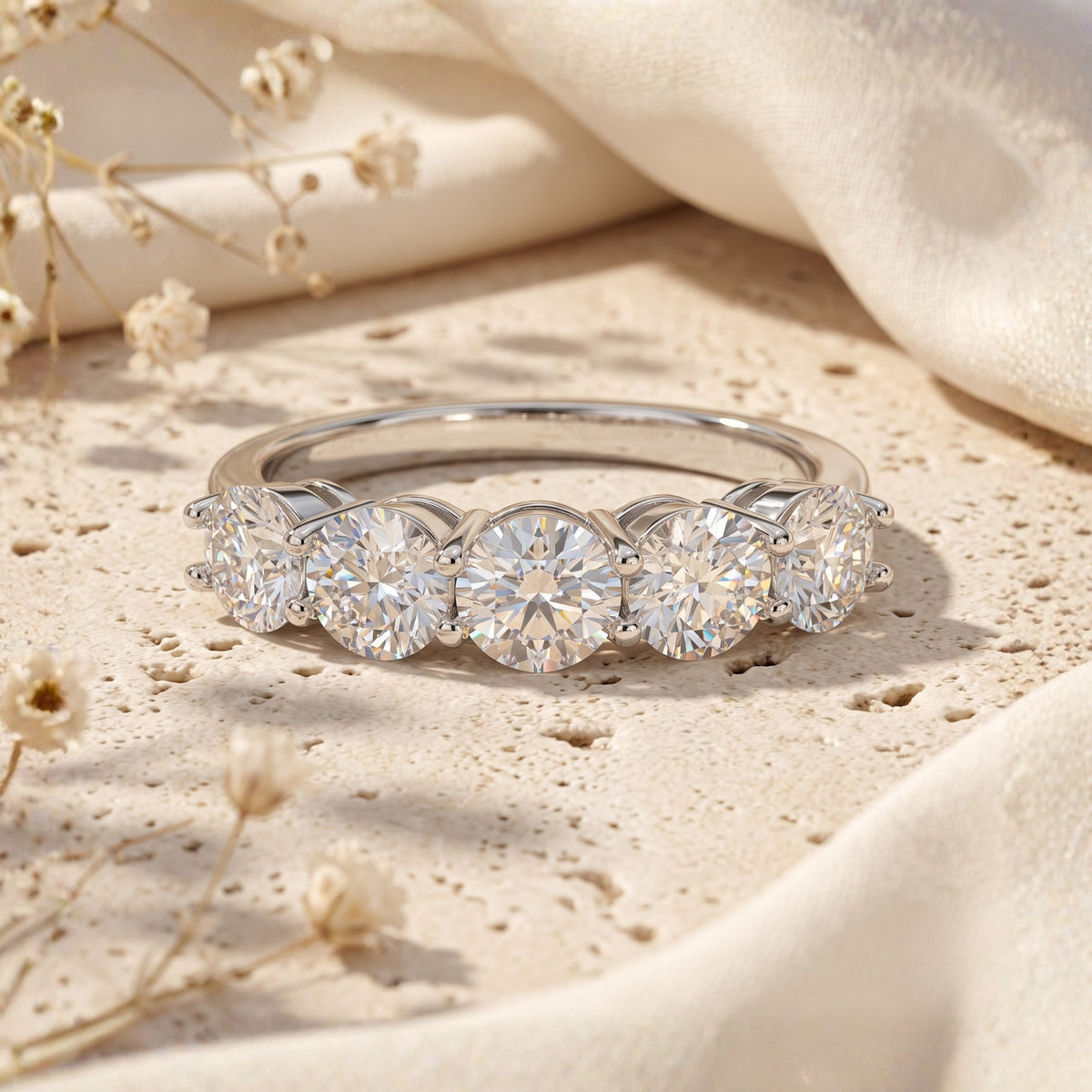 Front view of a silver ring set with a row of five round brilliant clear gemstones on textured stone.