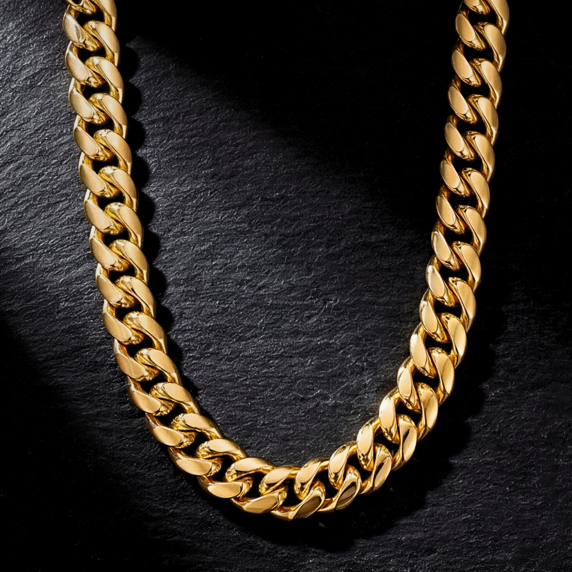 Top-down view of the gold 12mm Cuban link stainless steel chain on a dark textured stone surface.