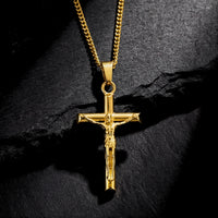Gold stainless steel Divine Cross crucifix pendant on a curb chain, resting on a dark textured stone surface.