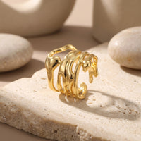 The Marinella Ring, a solid gold ring with a fluid silhouette, resting on a textured stone surface.