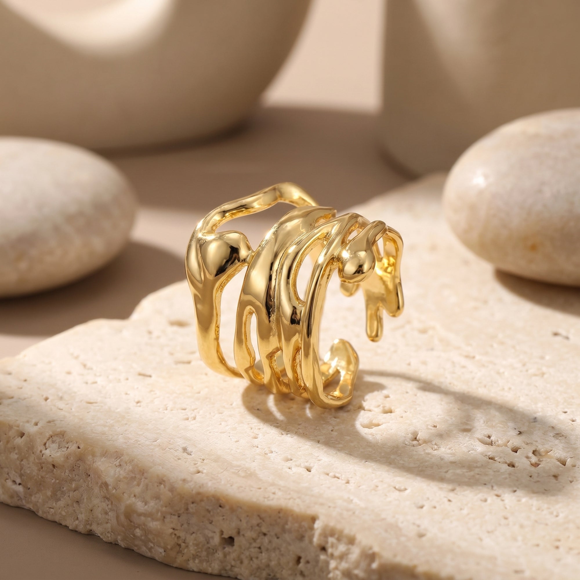 The Marinella Ring, a solid gold ring with a fluid silhouette, resting on a textured stone surface.
