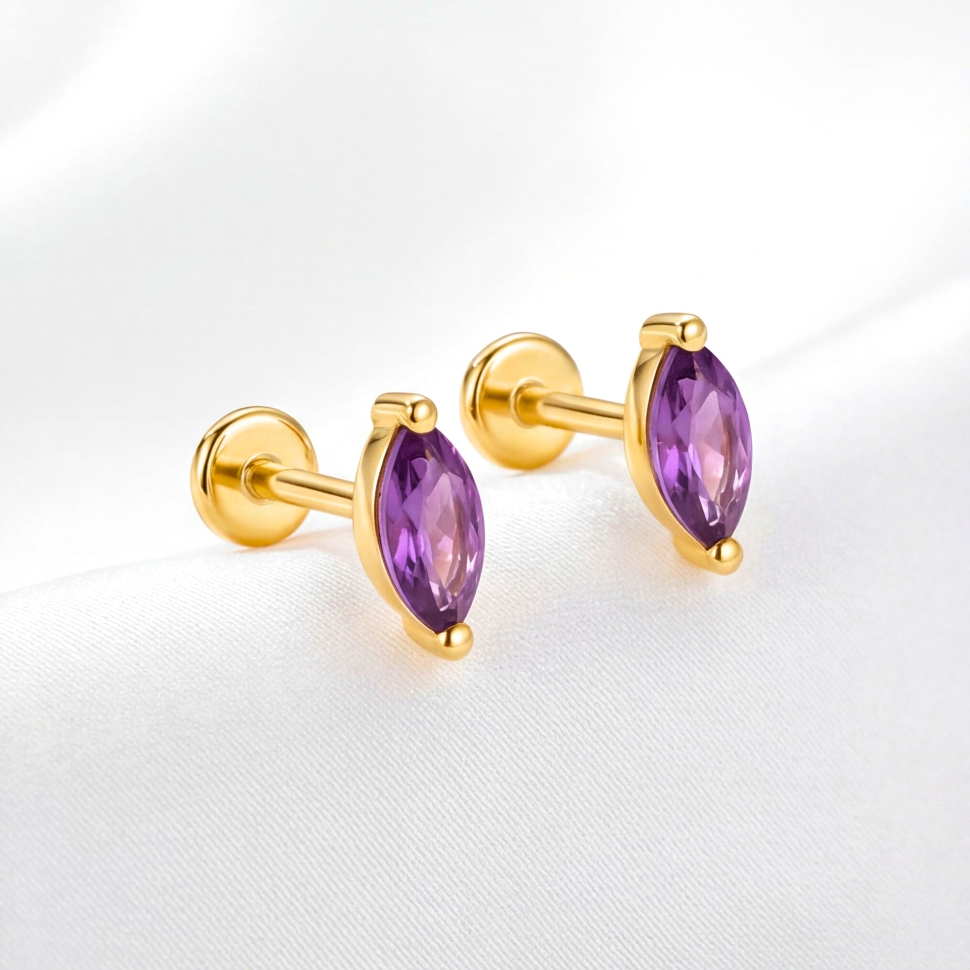 The Marcella Studs: marquise-cut purple simulated amethyst flat-back earrings in 18K gold vermeil on white fabric.
