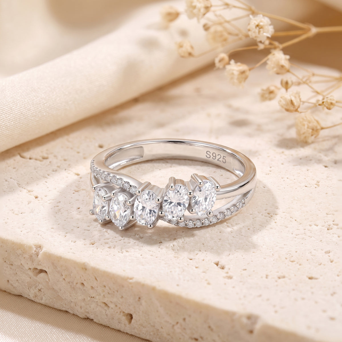 Sterling silver bypass ring with five oval-cut cubic zirconia stones and pavé accents, resting on a textured stone surface.