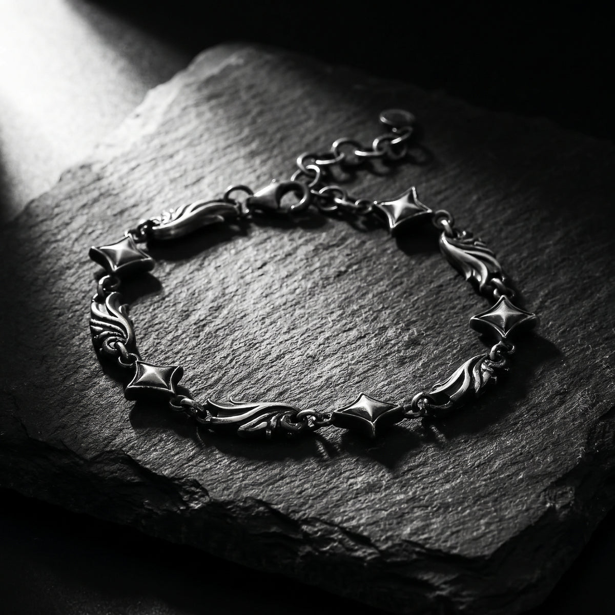Silver star and scroll link bracelet arranged in a loop on a dark slate slab under directional light.