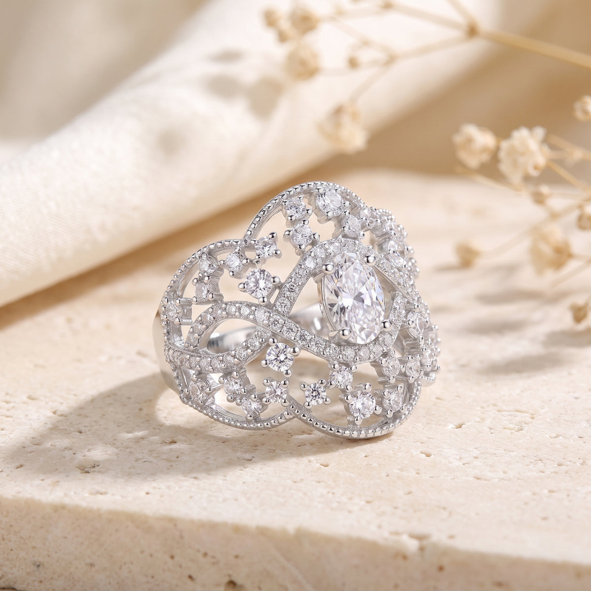 Silver openwork lace ring featuring an oval center stone and accent gems, resting on a textured stone surface.