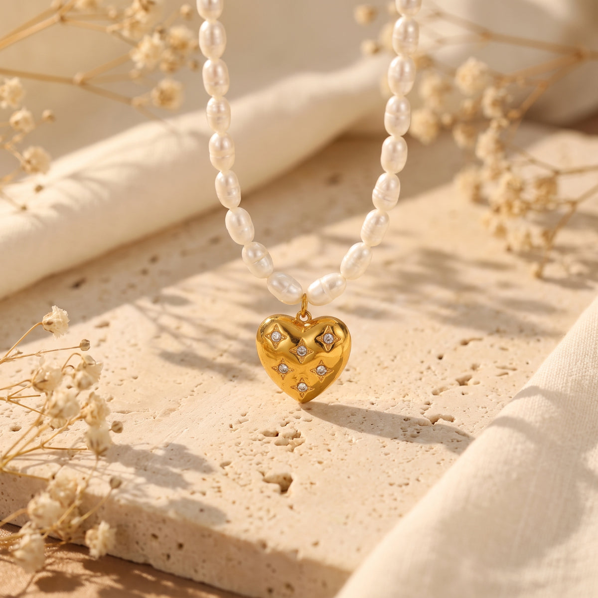 Close-up of a gold-tone heart pendant with cubic zirconia starbursts on a white pearl strand.
