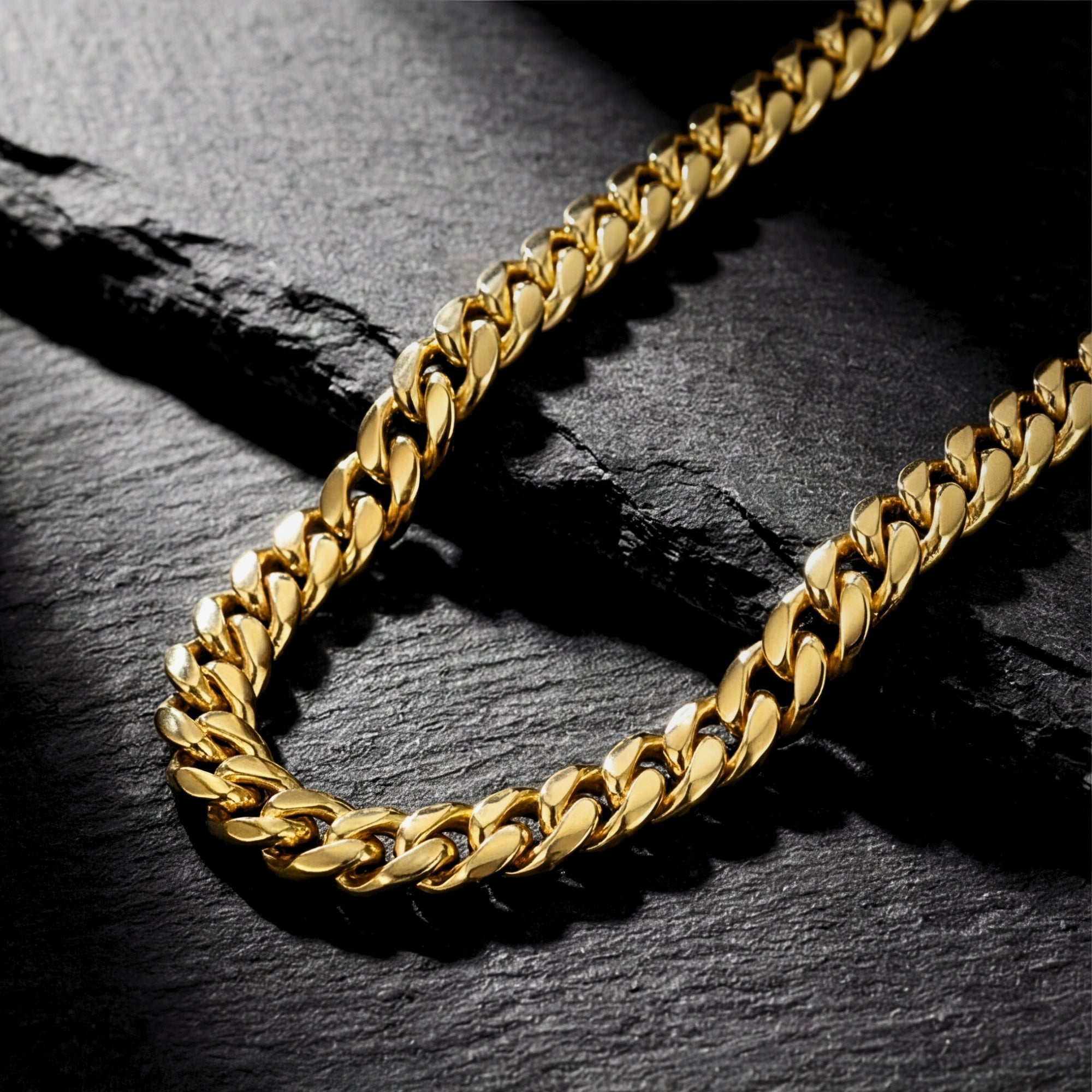 Close-up of a 6mm gold stainless steel Cuban chain resting on a dark, textured stone surface.