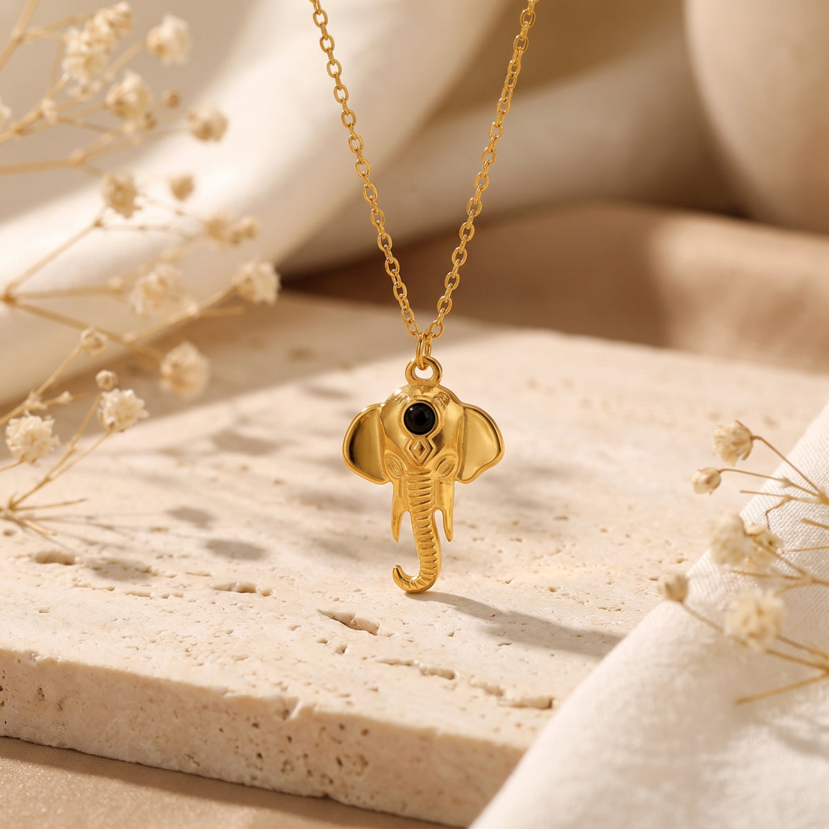 Gold-tone elephant pendant necklace with a black stone accent, hanging above a textured stone surface.