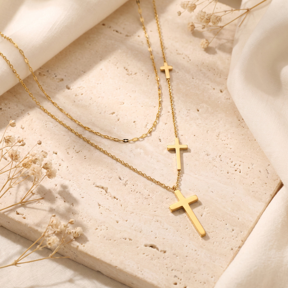 Gold-tone layered cross necklace with three cascading cross pendants displayed on a textured stone surface.