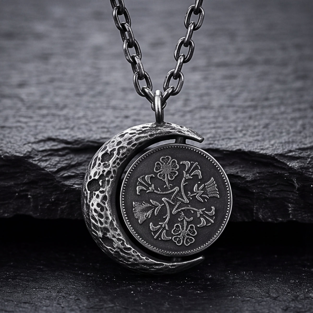 Front close-up of the silver lunar coin pendant with a cratered crescent frame and floral coin motif on dark slate.