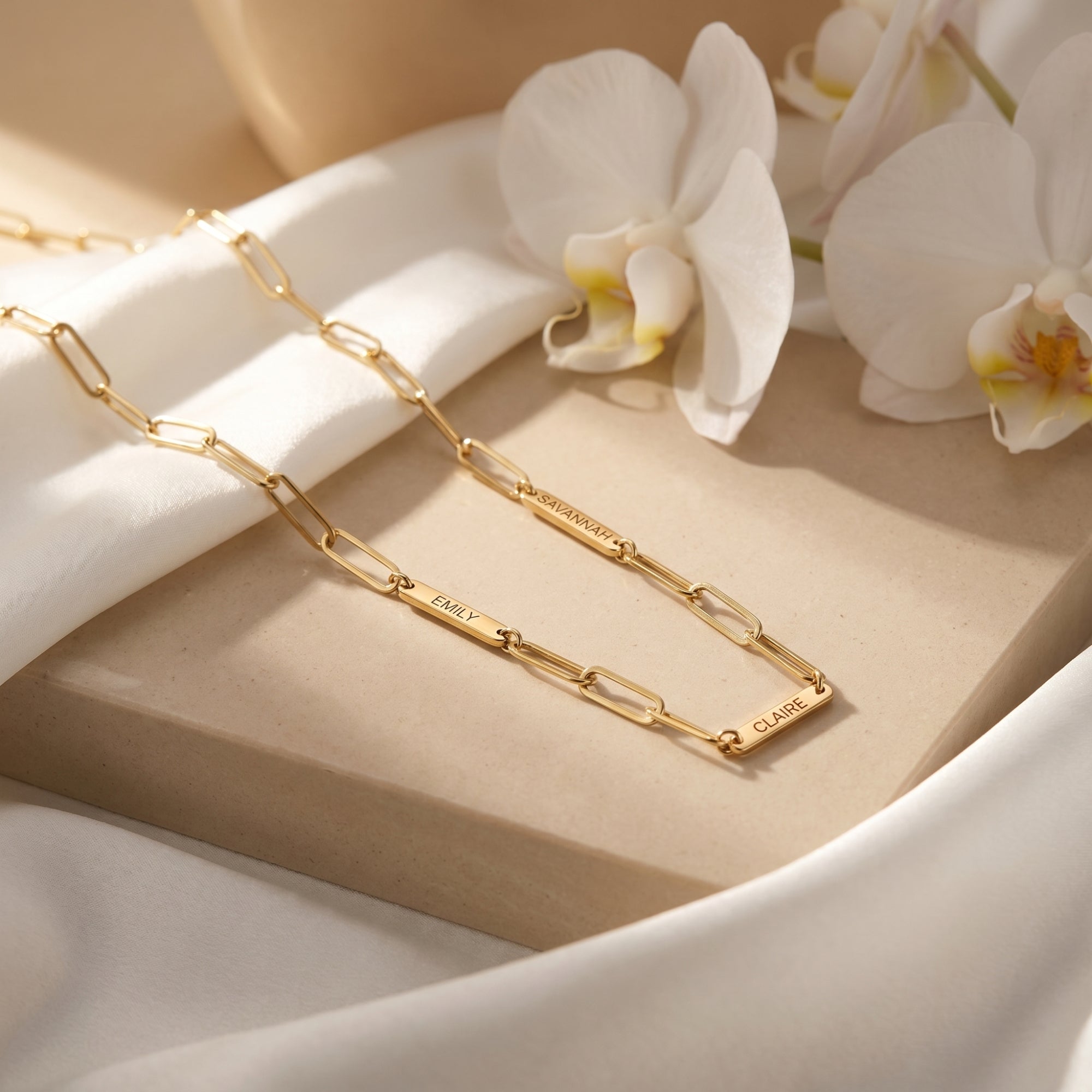 Gold stainless steel paperclip name necklace on stone with orchids.