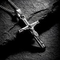 Polished silver stainless steel crucifix pendant shown in a detailed macro shot on a dark stone background.