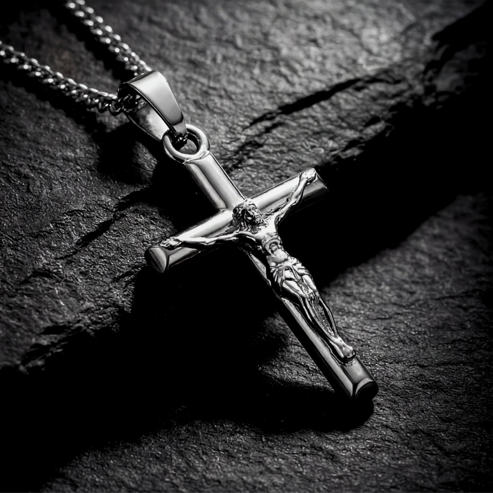 Polished silver stainless steel crucifix pendant shown in a detailed macro shot on a dark stone background.