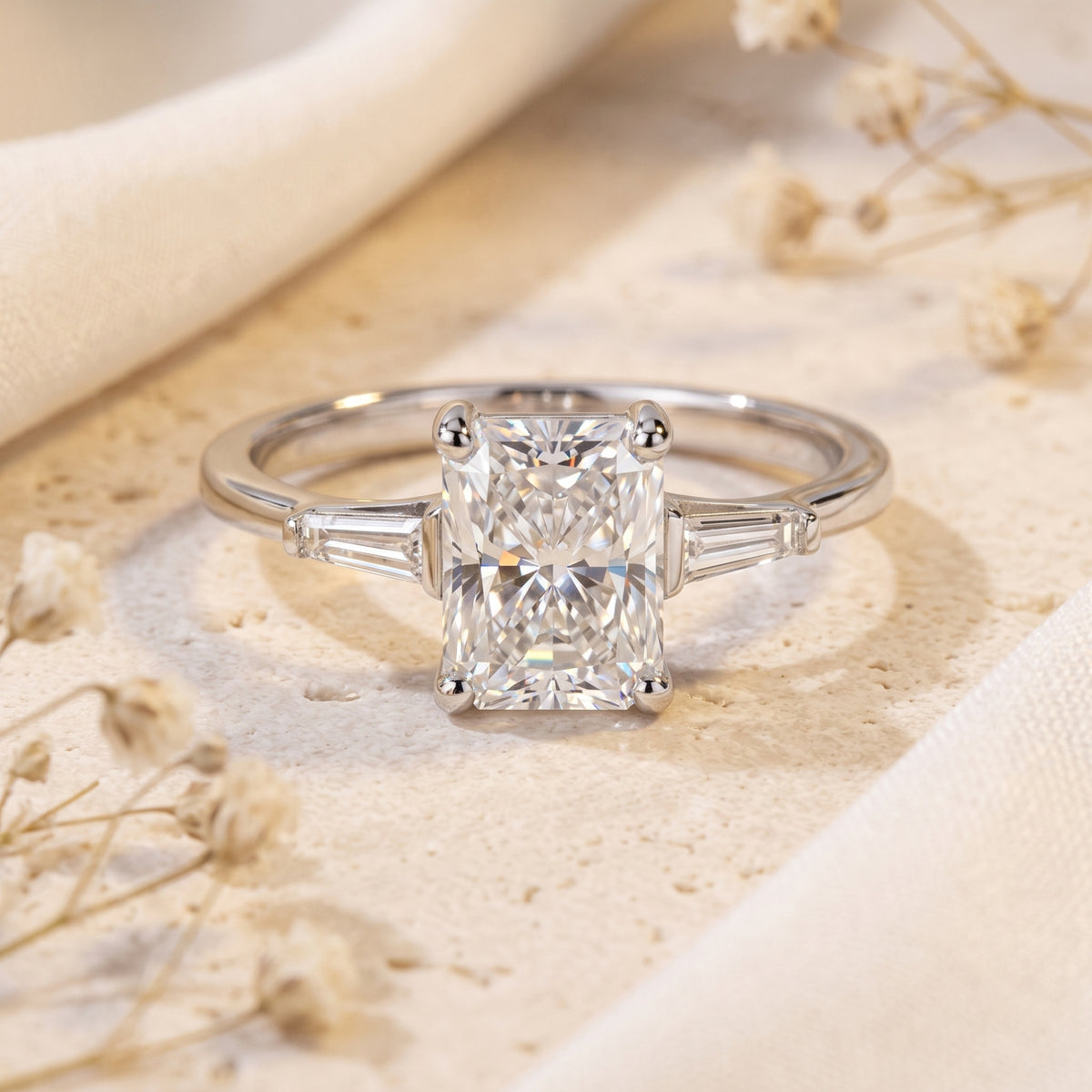 Front view of a silver three-stone ring featuring a radiant-cut center stone and tapered baguette accents.