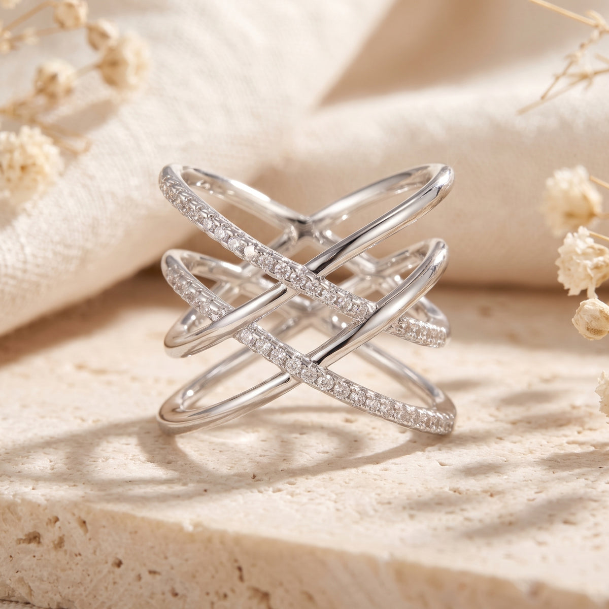 Front view of a silver multi-band crossover ring with pavé stones standing on a textured stone surface.