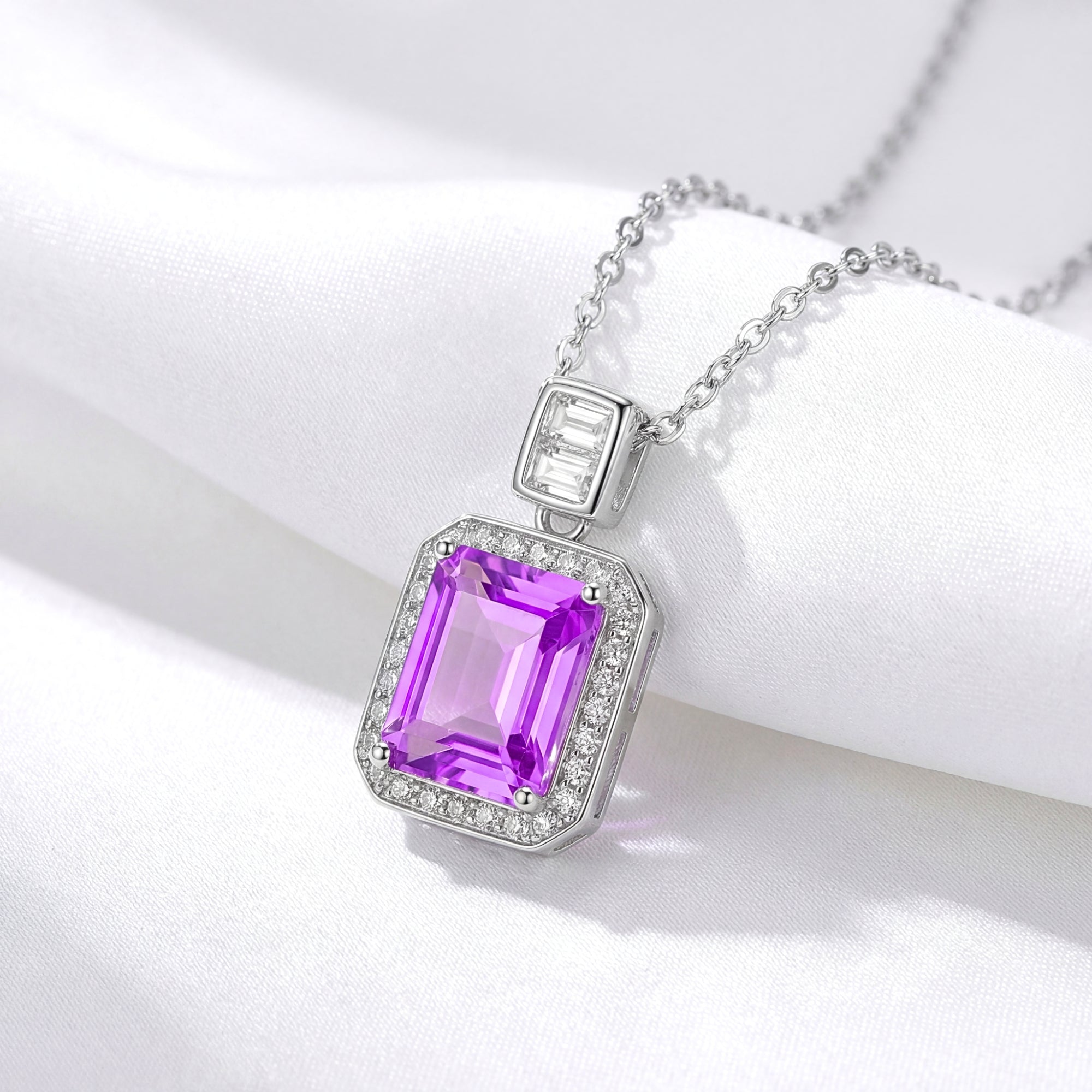 Emerald cut purple simulated amethyst pendant in sterling silver on a white draped fabric background.