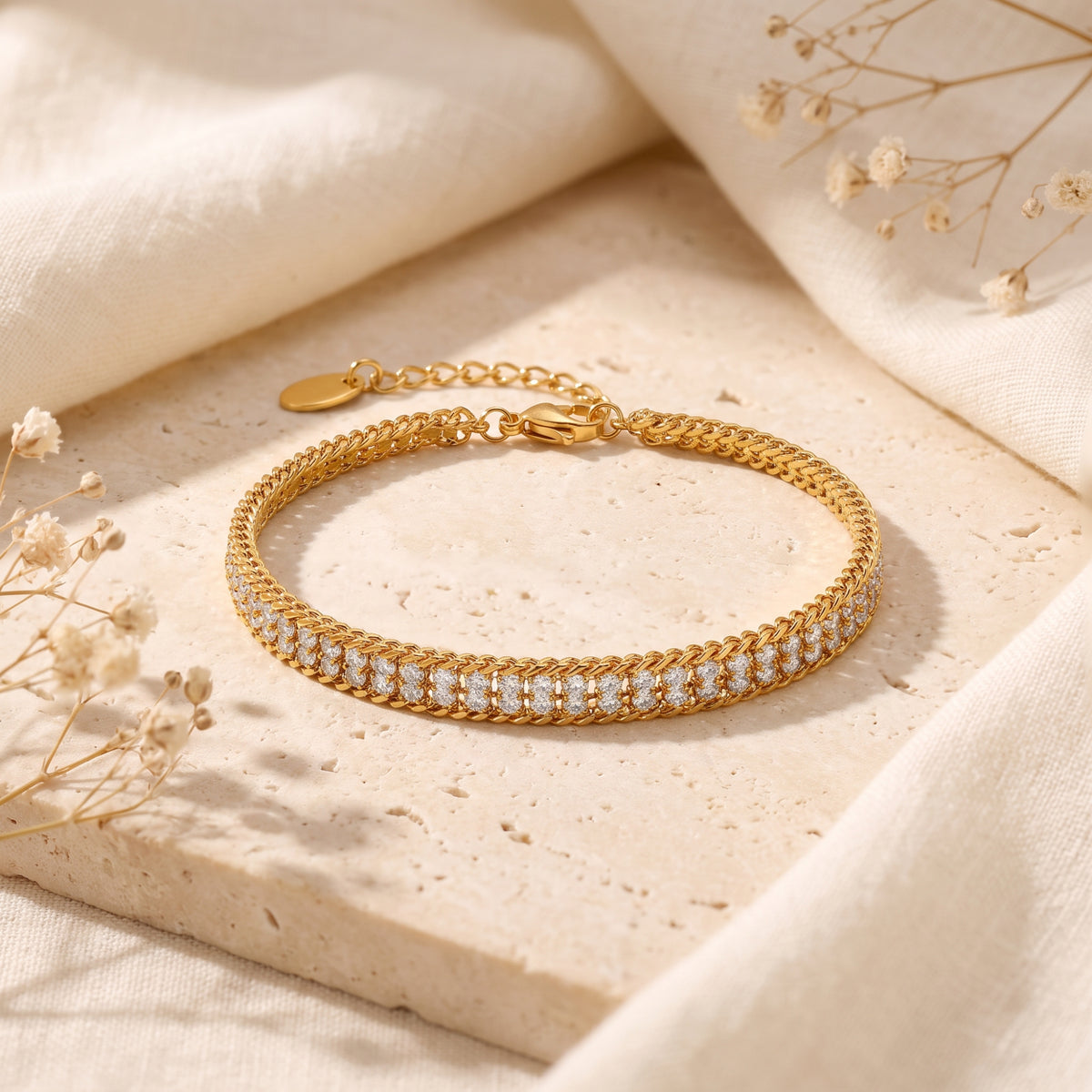 Gold-tone double-row pavé link bracelet laid flat on a textured stone slab with clasp and extension chain visible.