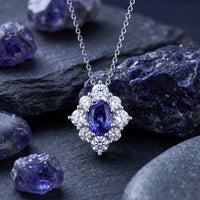 Oval natural tanzanite halo pendant in white gold on a silver chain, displayed with raw tanzanite stones.