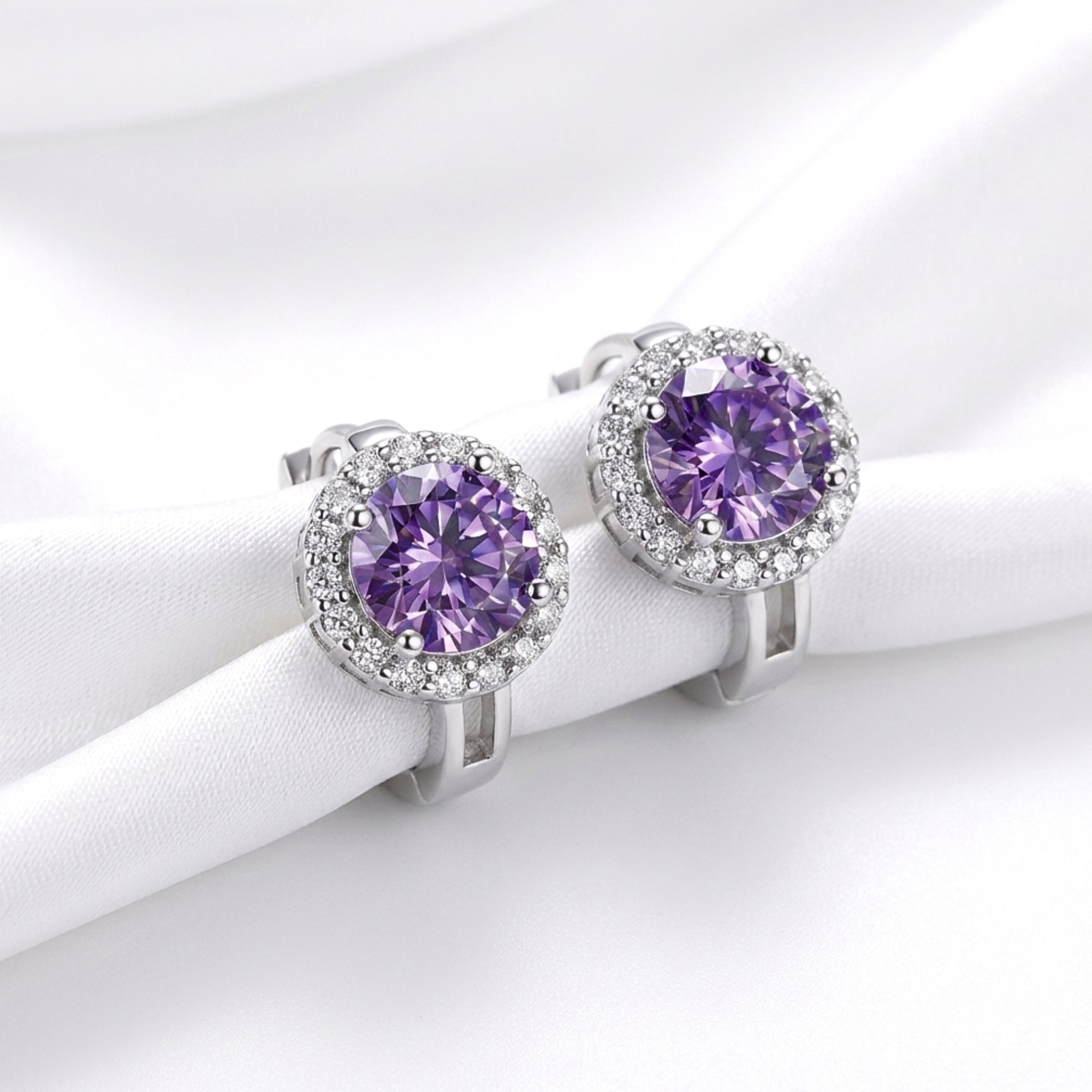 Front view of round cut purple moissanite halo earrings in S925 sterling silver on white fabric.