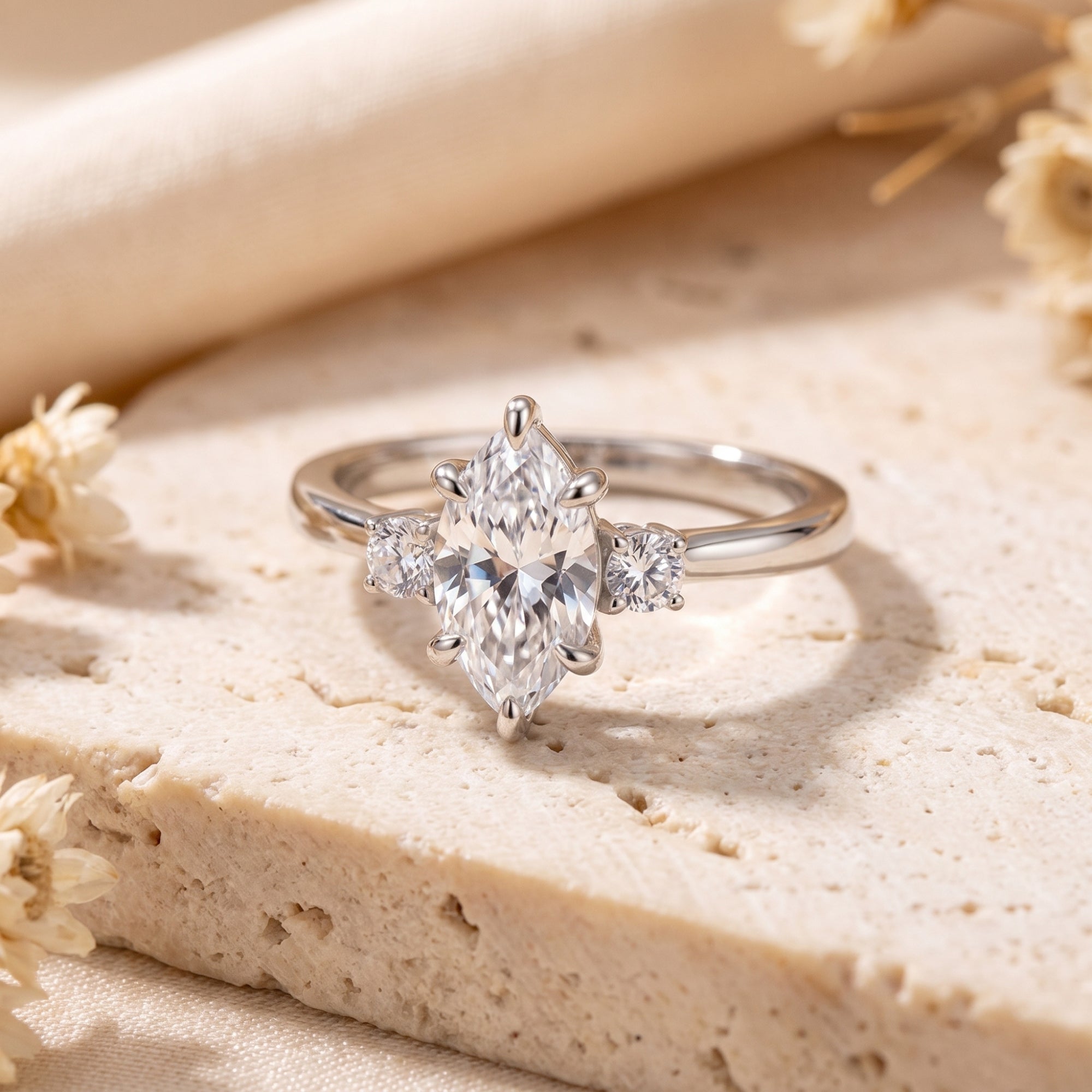 Marquise-cut simulated diamond silver promise ring on a stone surface with dried flowers.